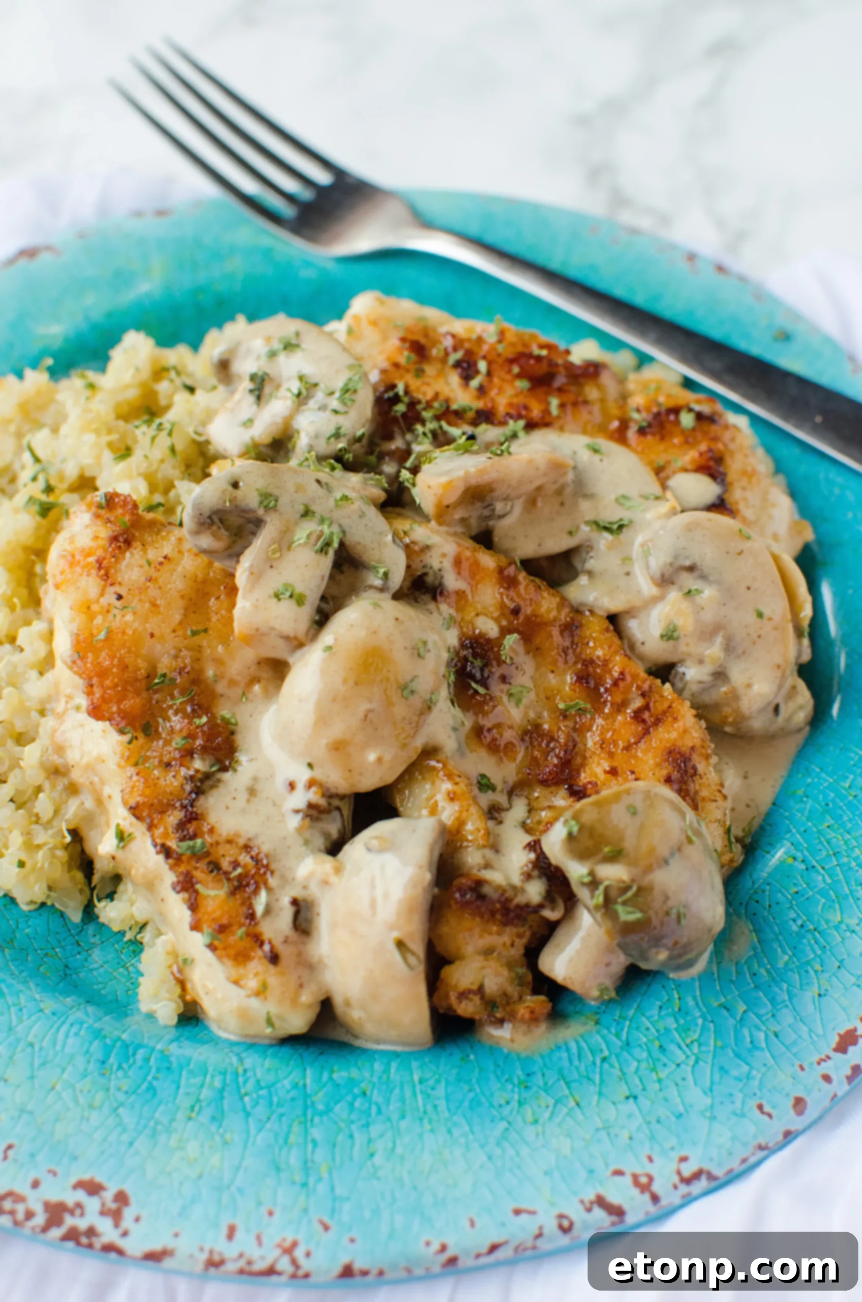 A close-up of a chicken piece covered in thick Asiago sauce