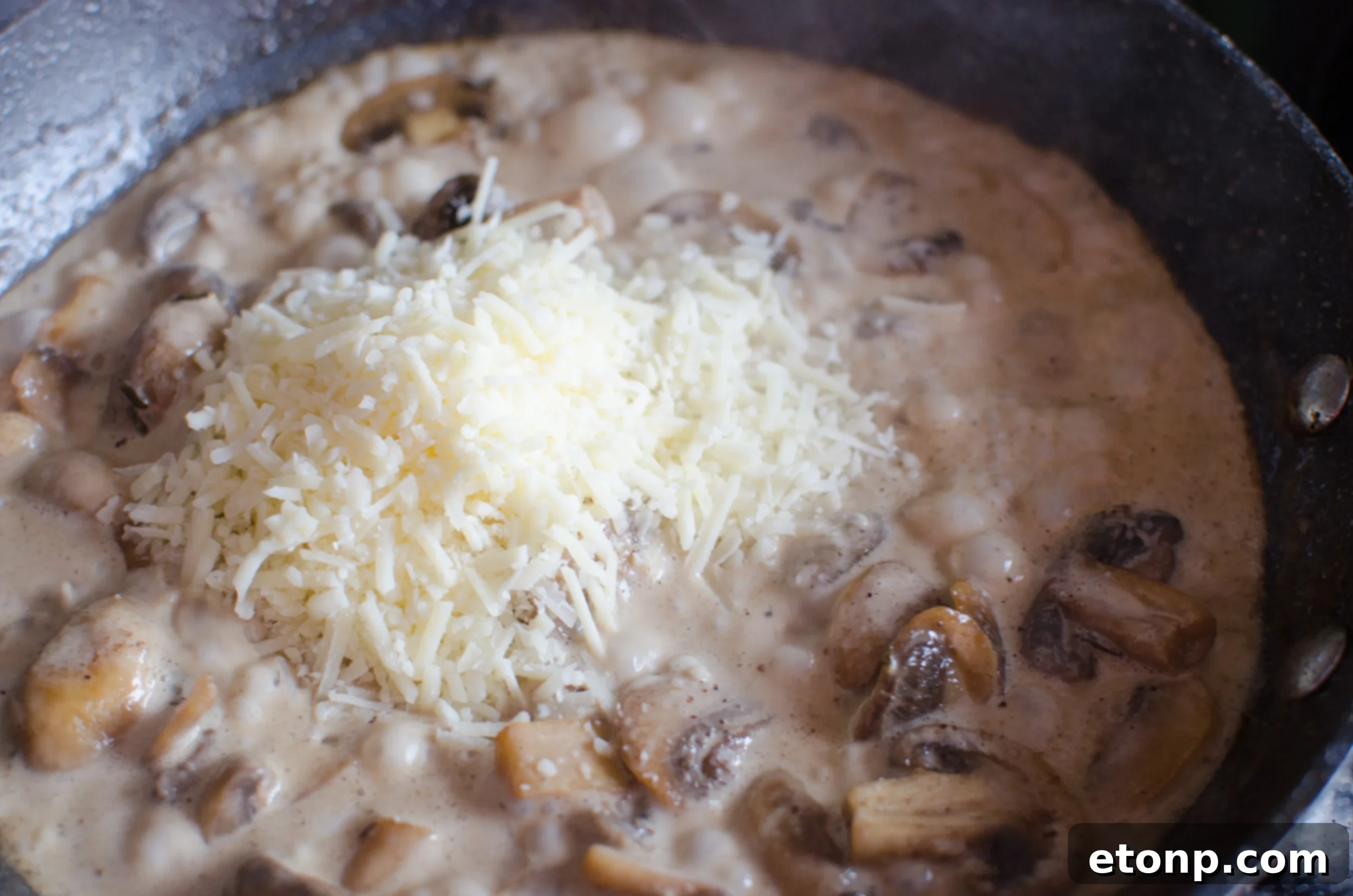 Fresh mushrooms being sauteed in a skillet, part of the Asiago chicken recipe