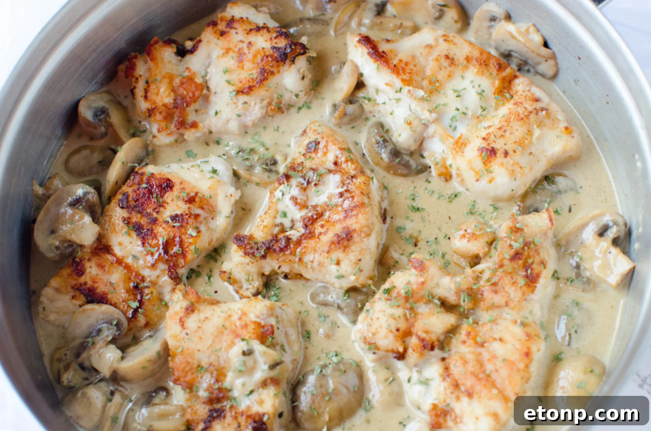 Close-up of chicken breasts simmering in a creamy white wine sauce