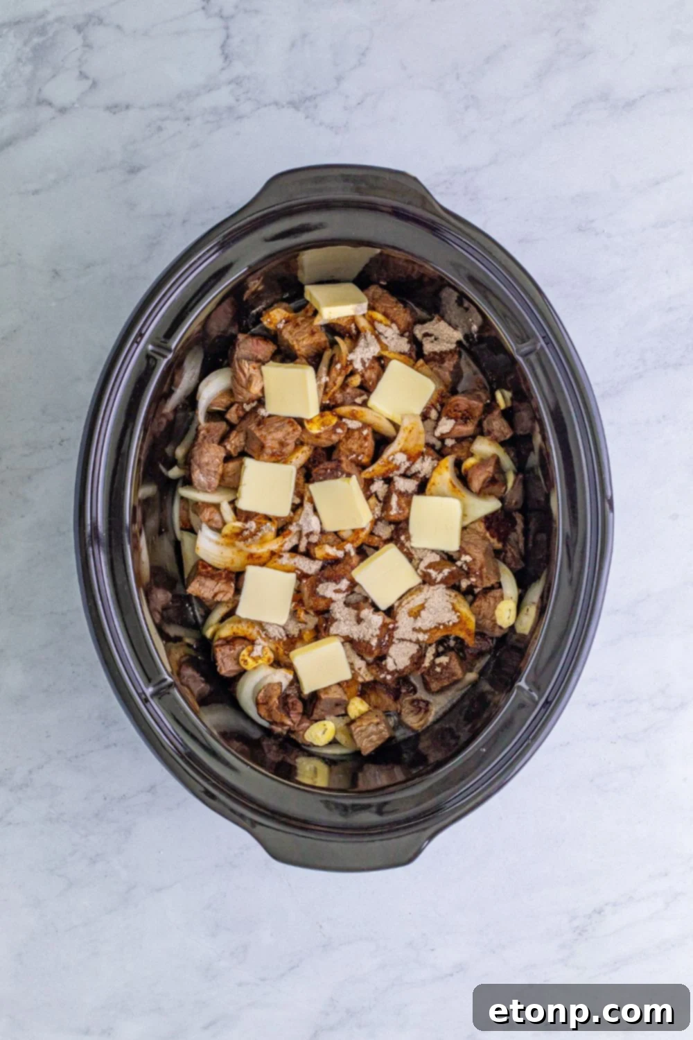 steak bites and mixture in a crockpot with slices of butter on top 