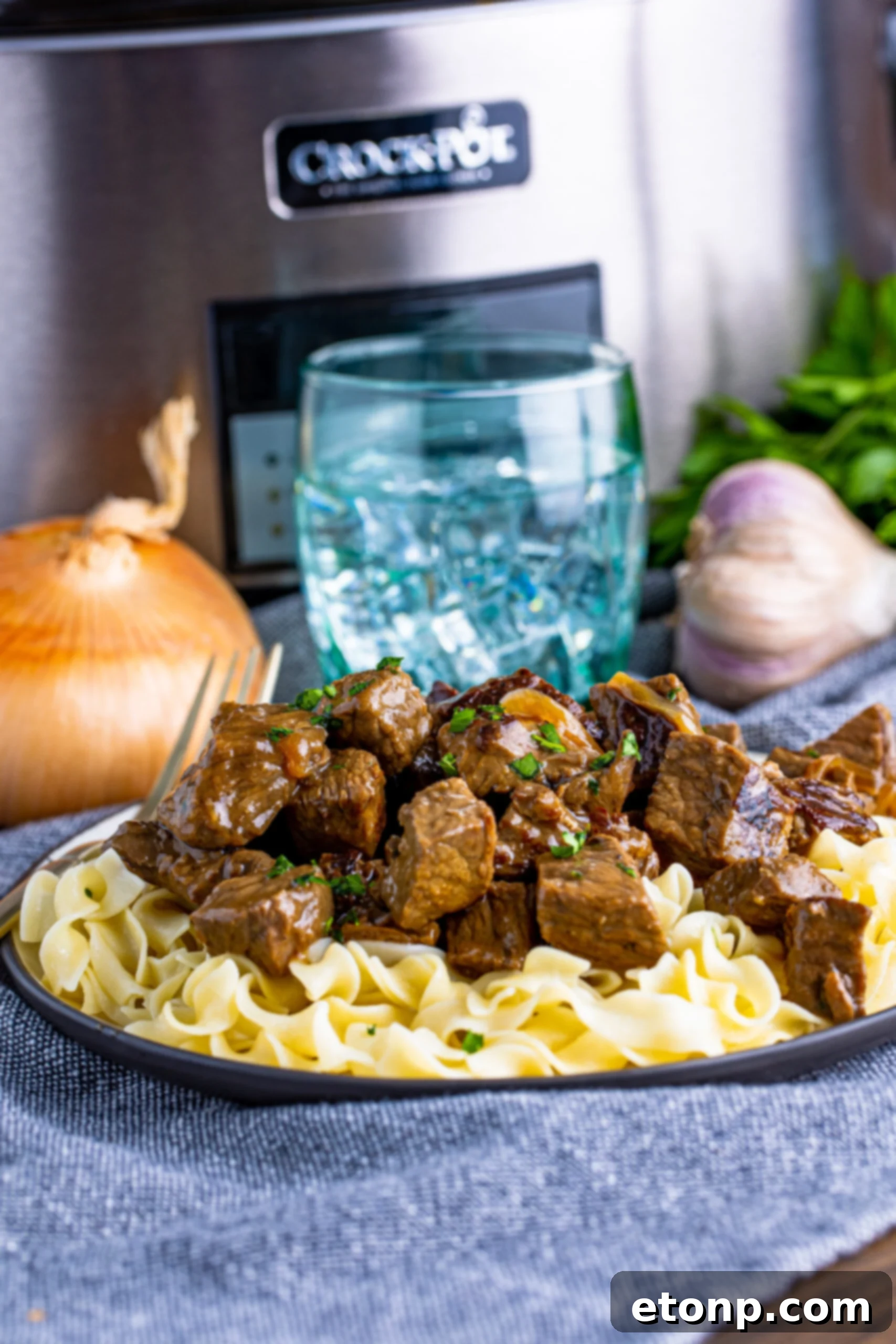 steak and noodles on plate with onion and a glass behind it on table