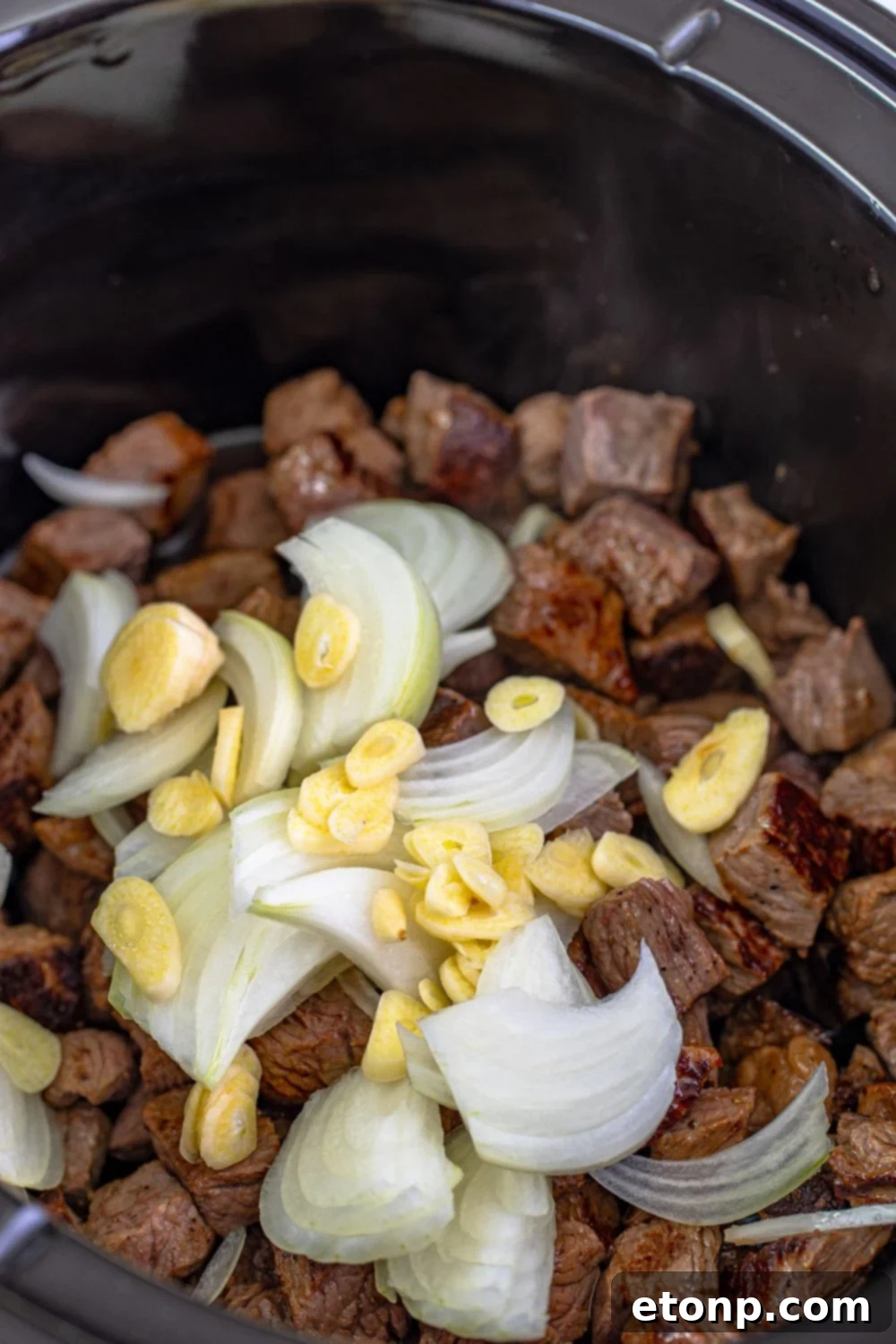 garlic and onions on top of seared steak in a crockpot 