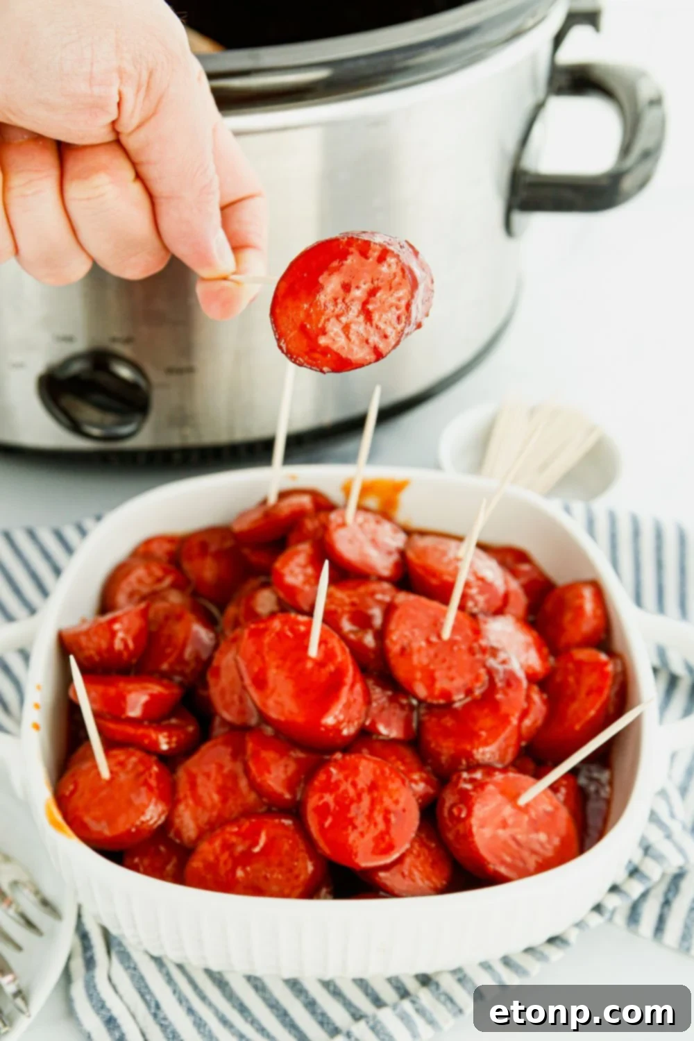 A hand holding a toothpick with a perfectly glazed kielbasa bite, highlighting its appetizer appeal.
