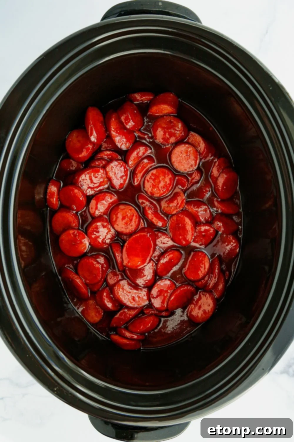 An overhead shot revealing a slow cooker brimming with perfectly cooked and coated kielbasa bites, swimming in their rich sauce.