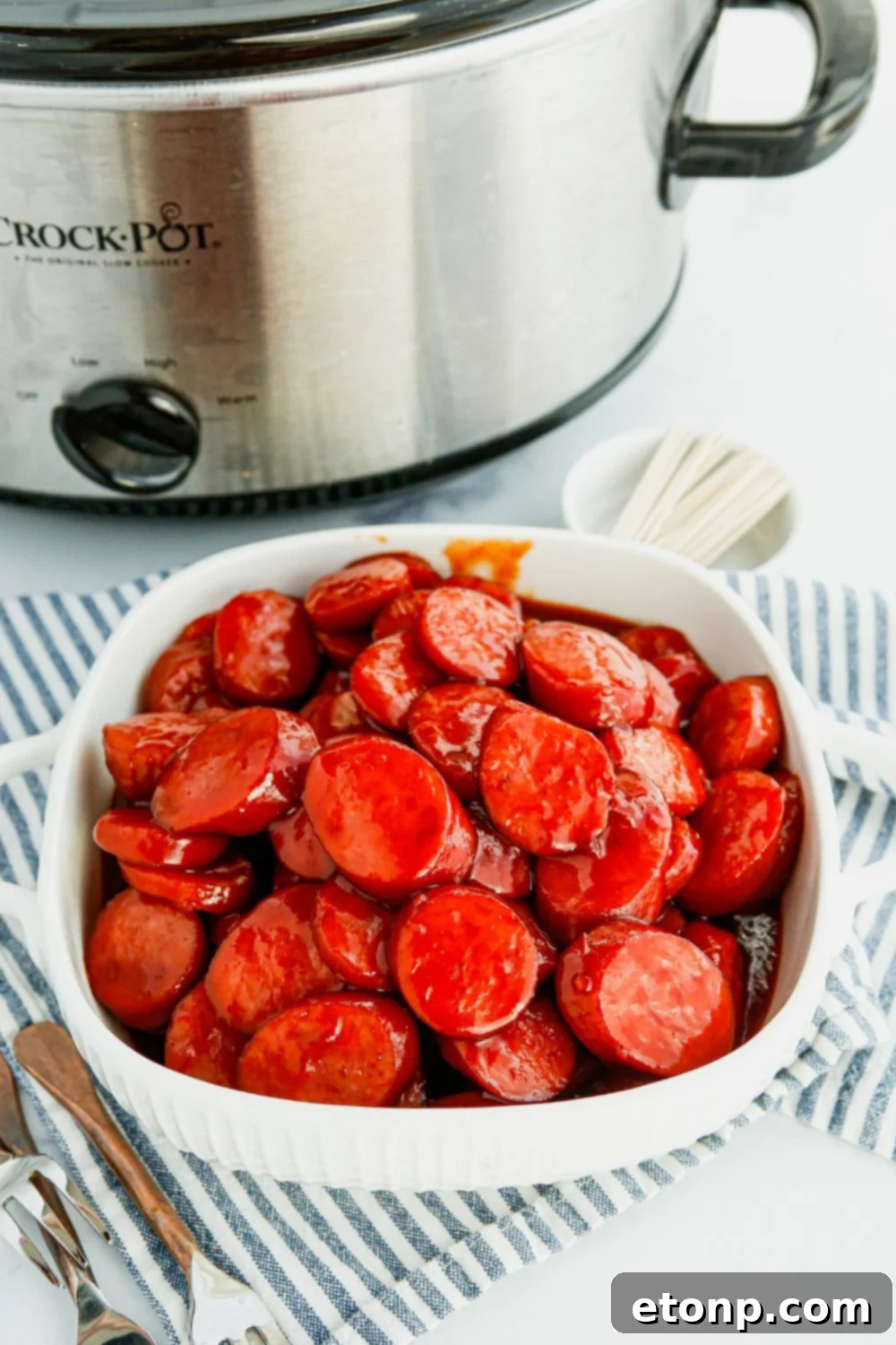 A serving bowl filled with saucy kielbasa bites sits beside a slow cooker, illustrating easy serving straight from the pot.