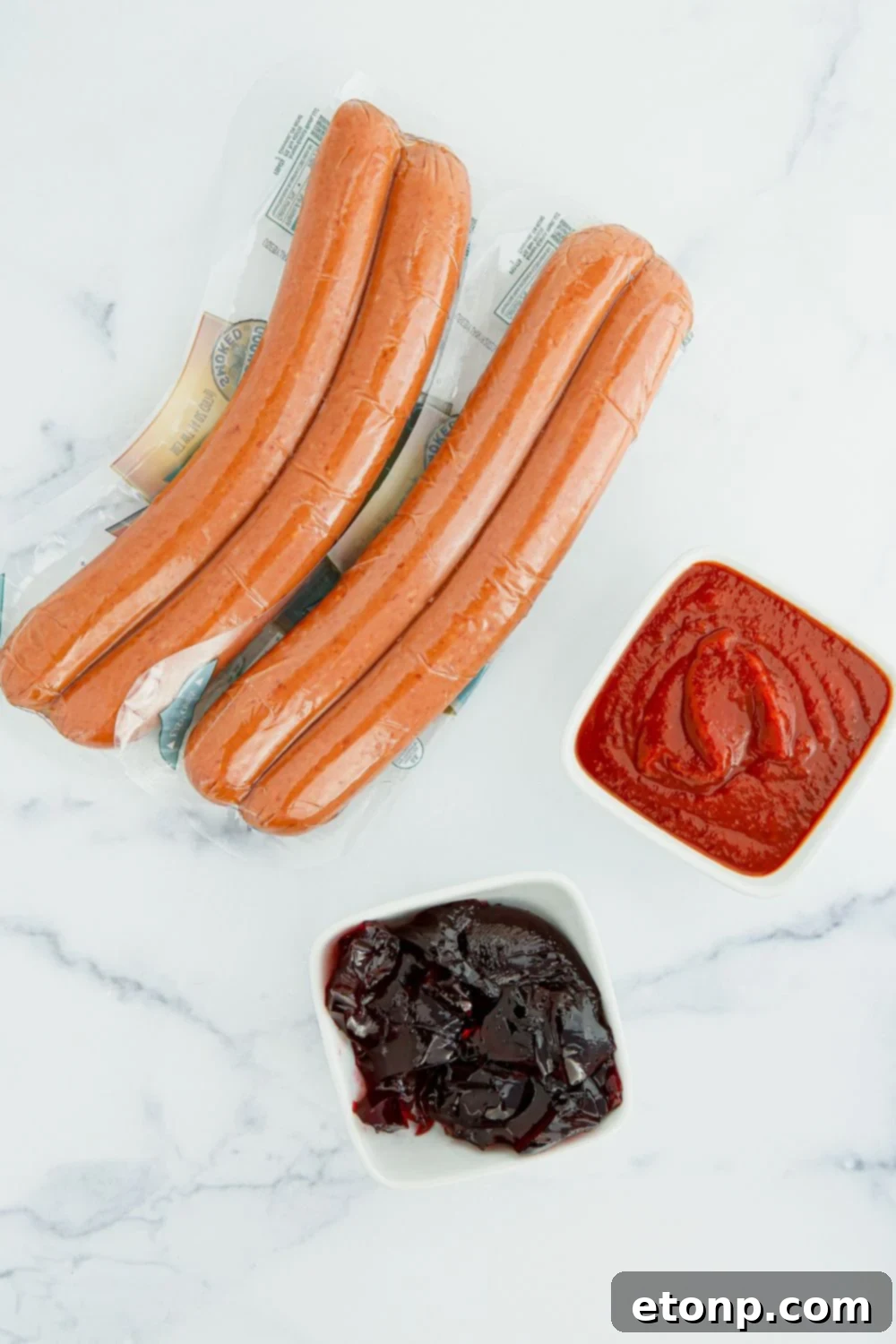Fresh kielbasa sausage laid out on a table, with bowls of vibrant chili sauce and luscious grape jelly beside it, highlighting the simple ingredients.