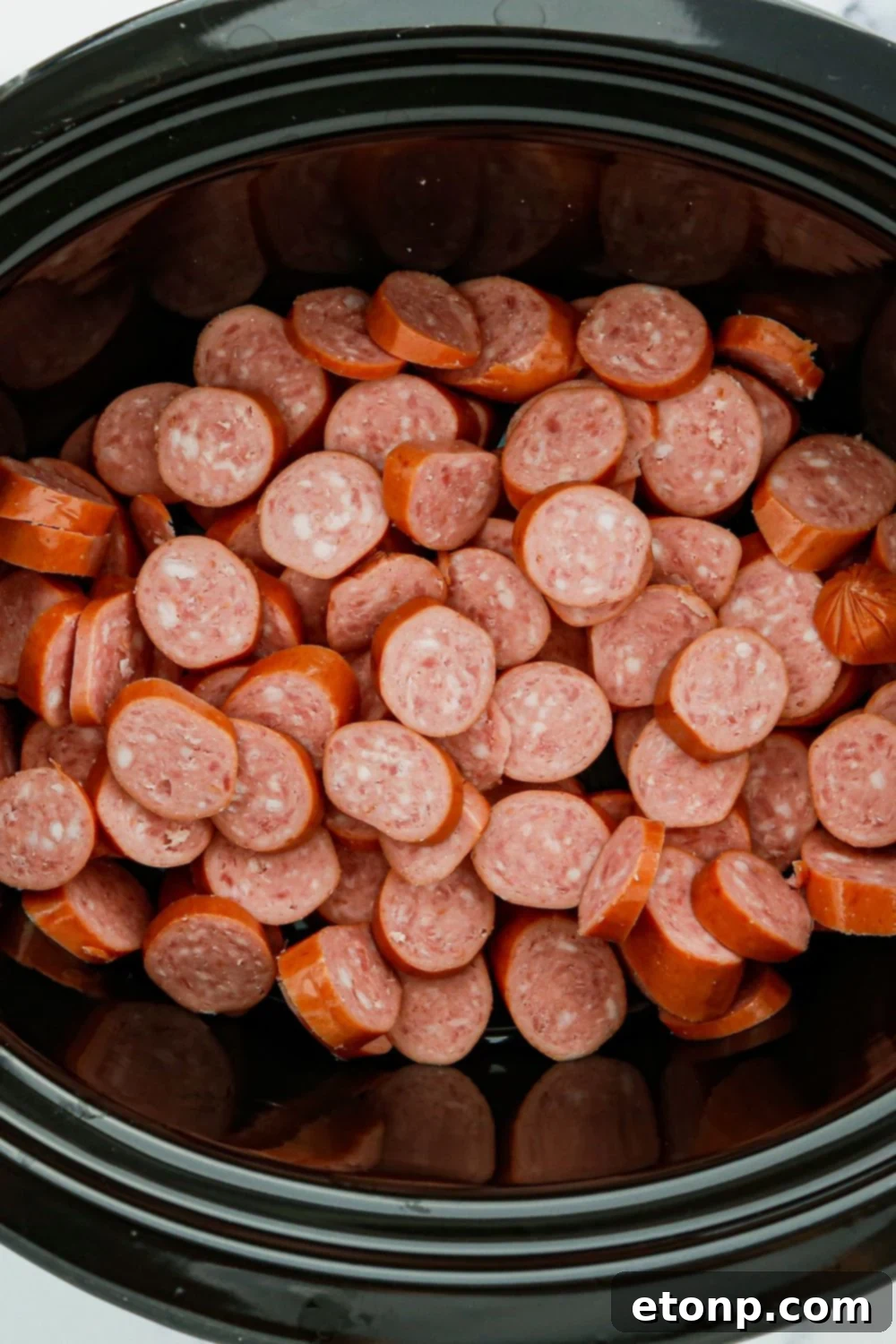 Neatly sliced smoked sausage resting at the bottom of a crockpot, awaiting its flavorful sauce.