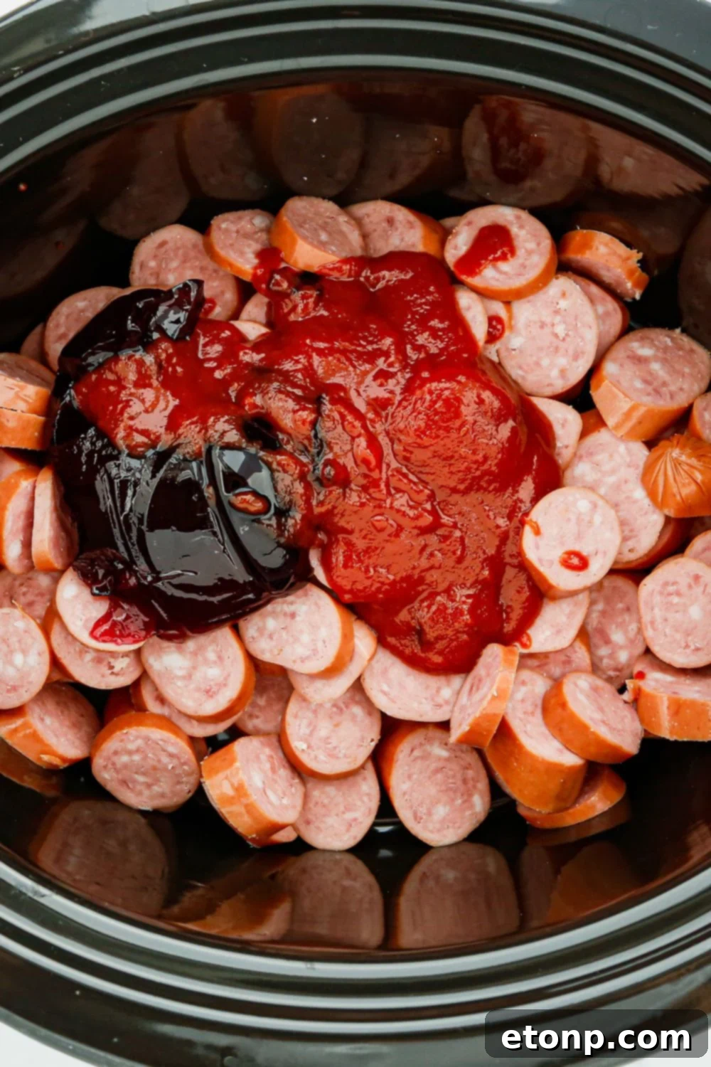 The three essential ingredients for crockpot kielbasa: sliced sausage, a bottle of chili sauce, and a jar of grape jelly, arranged on a surface.
