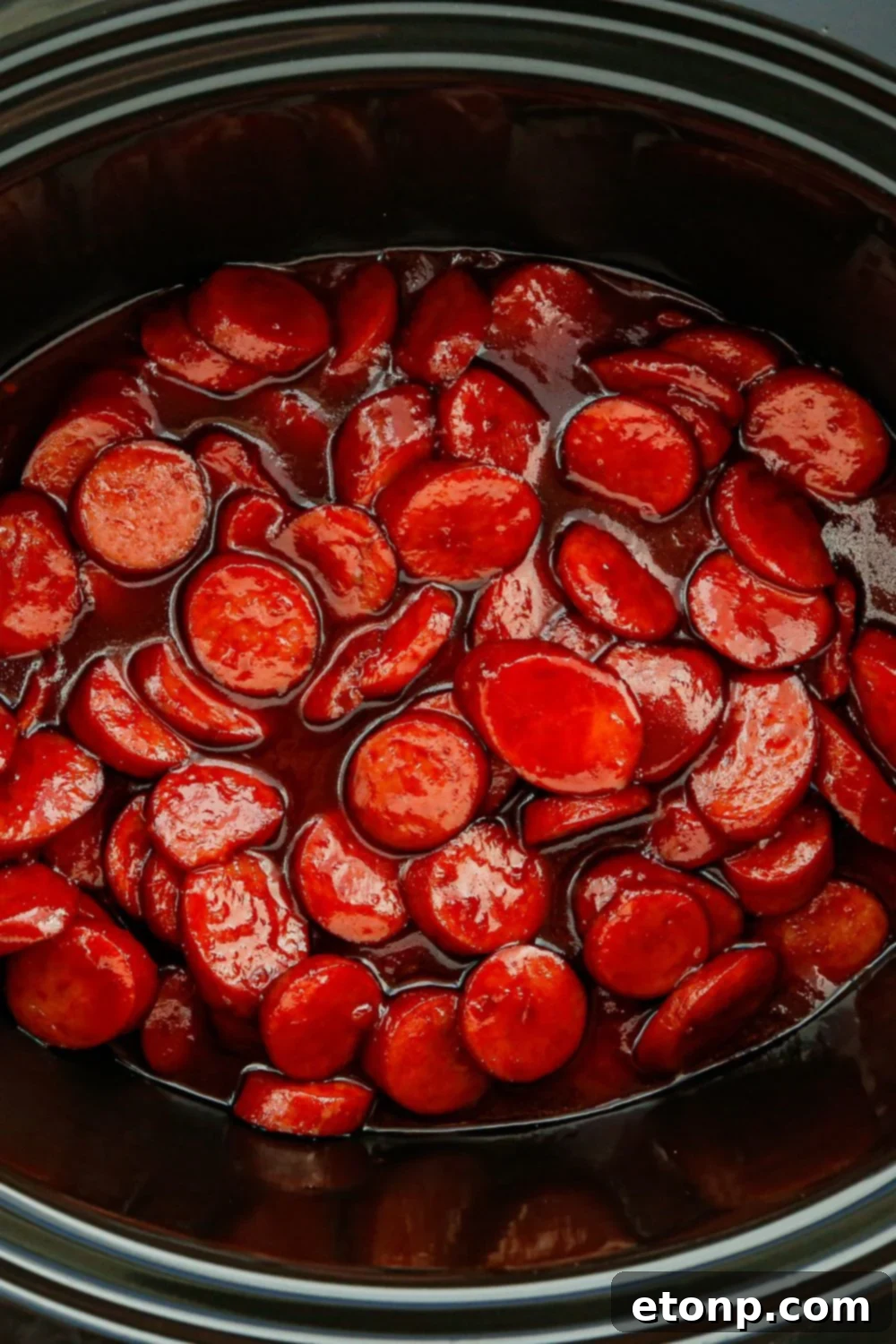A slow cooker filled with glazed kielbasa bites, gently simmering and filling the air with an enticing aroma, set on a wooden table.