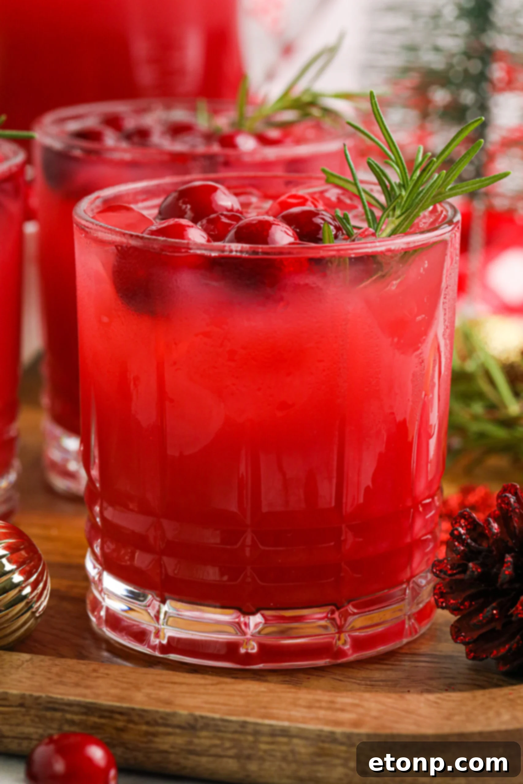 Close-up of a glass of Mistletoe Punch, garnished with fresh cranberries and a rosemary sprig, sparkling with holiday cheer.