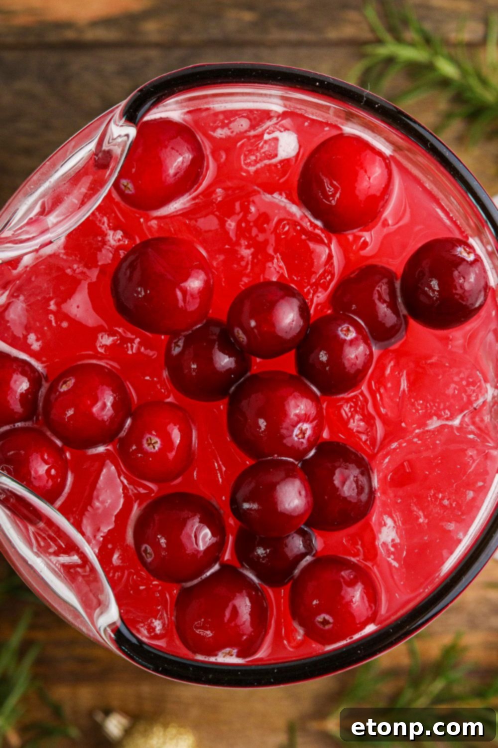 An inviting overhead shot of Mistletoe Punch in a large punch bowl, adorned with floating cranberries and rosemary sprigs.