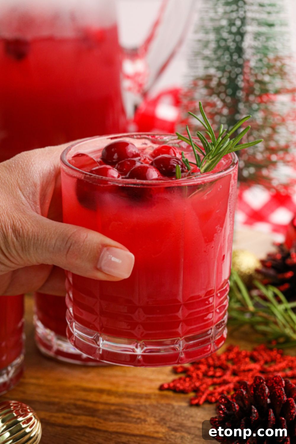 A hand holding a glass of vibrant Mistletoe Punch, surrounded by soft holiday lighting, capturing the essence of festive cheer.