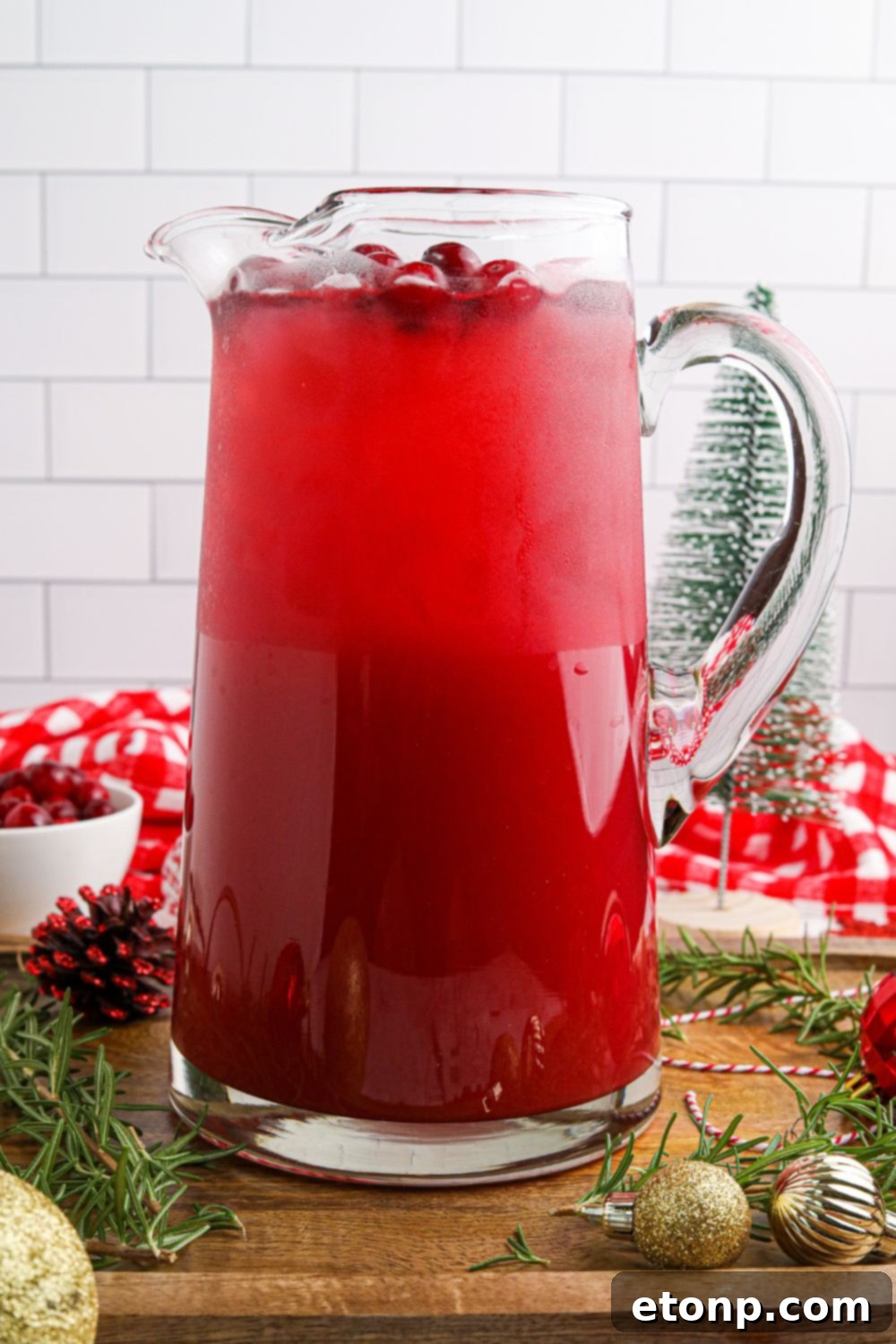 A large pitcher filled with vibrant Mistletoe Punch, garnished with fresh cranberries and rosemary, ready to be served.