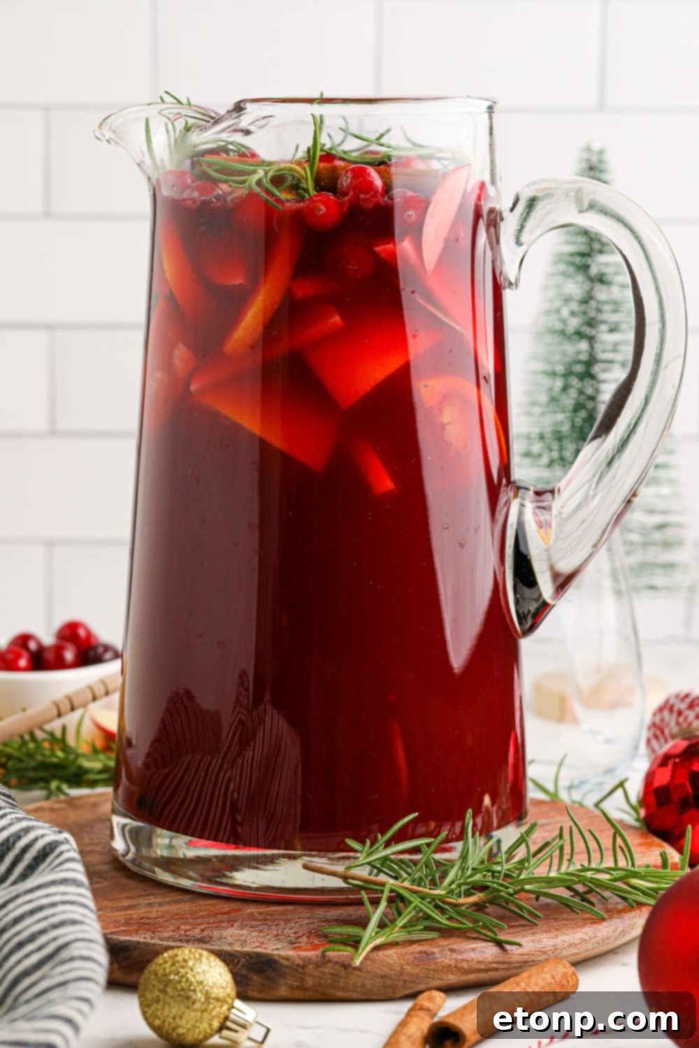 Cranberry Apple Christmas Sangria in a glass pitcher on table with garnishes around it 