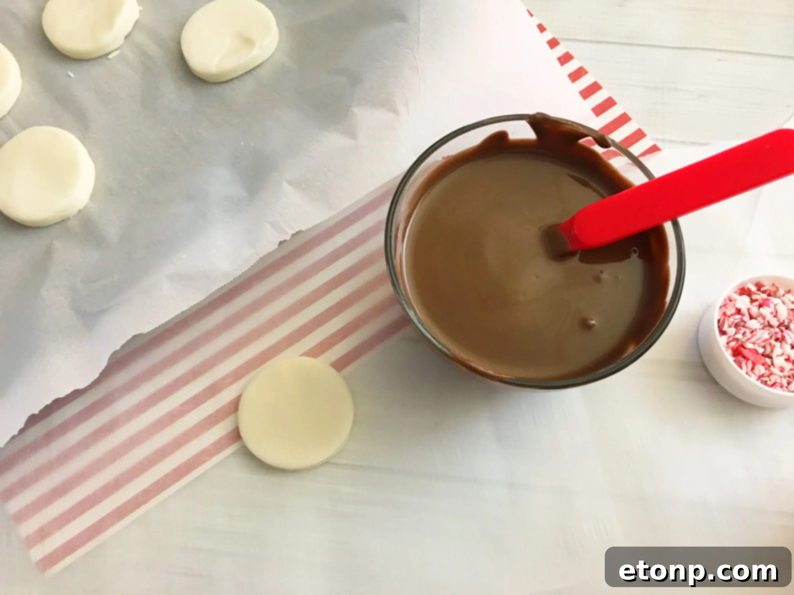 Rows of freshly dipped peppermint patties on parchment paper, some already sprinkled with crushed peppermint.