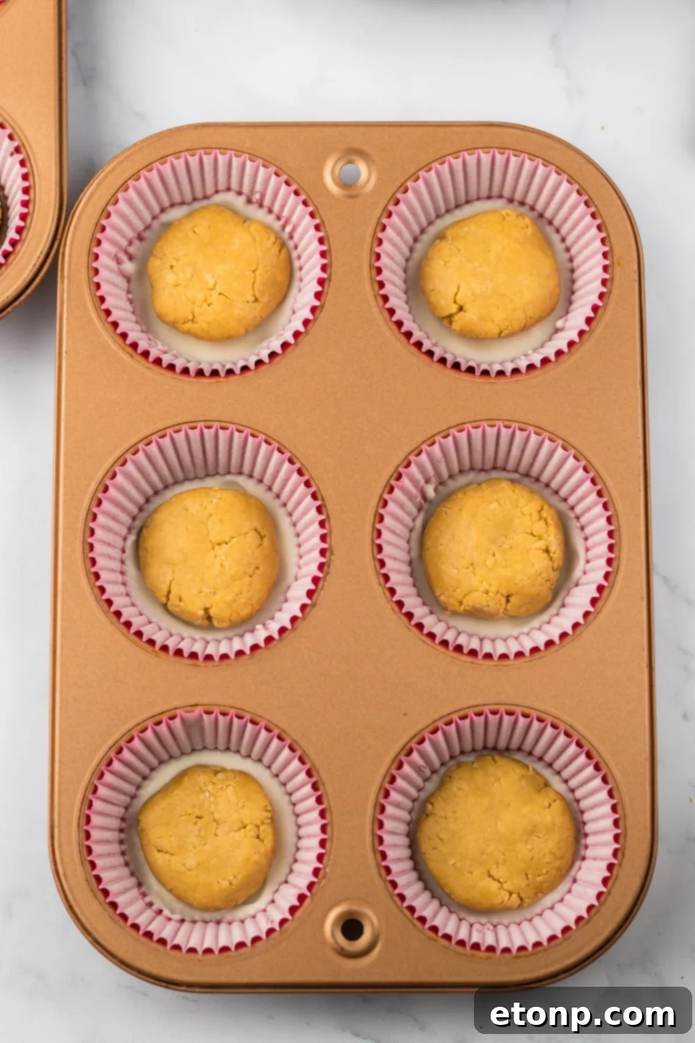 Balls of peanut butter on top of chocolate in a muffin tin