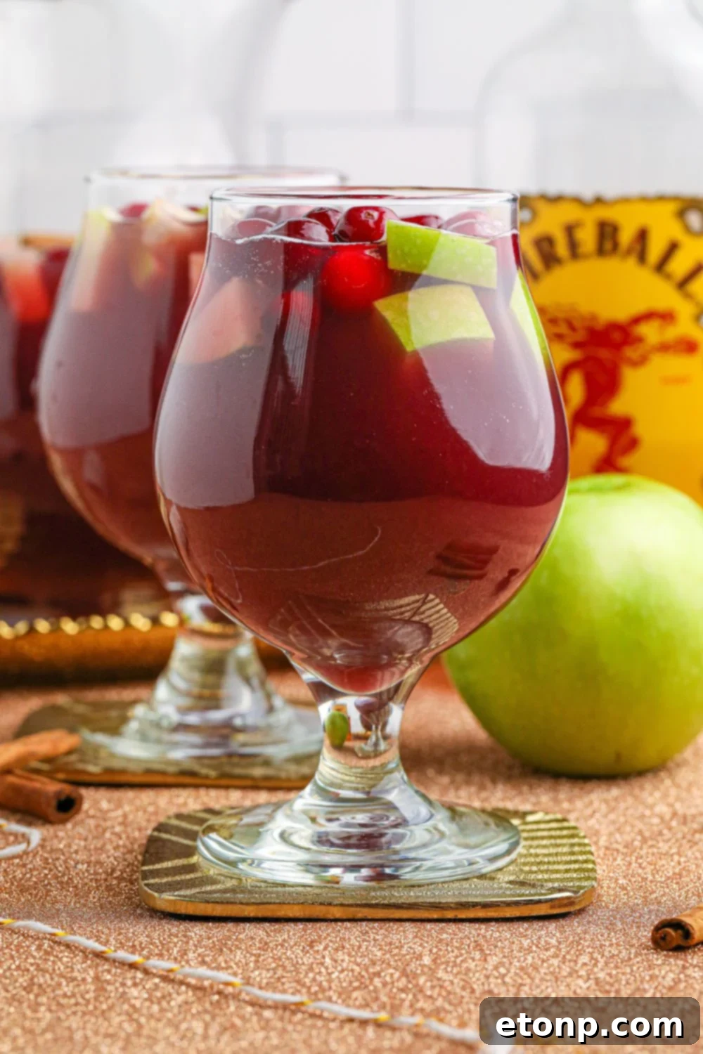 Cinnamon Spice Sangria 12 Side view of two glasses of Fireball Sangria on a table, with an apple and a Fireball whiskey bottle blurred in the background, suggesting a perfect pairing.