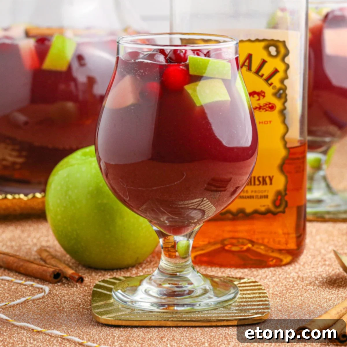Cinnamon Spice Sangria 3 Two glasses of Fireball Sangria with sliced apples and cranberries, accompanied by a bottle of Fireball whiskey and an apple in the background.