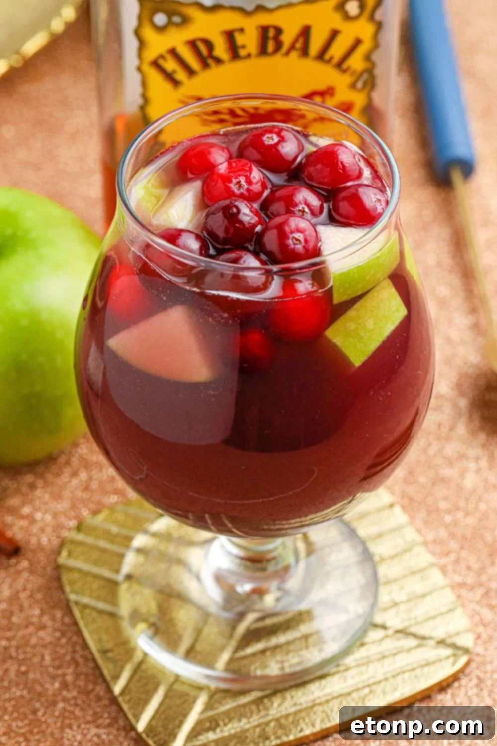 Cinnamon Spice Sangria 8 A glass of Fireball Sangria with an apple in the soft-focus background, emphasizing the drink's fresh ingredients.