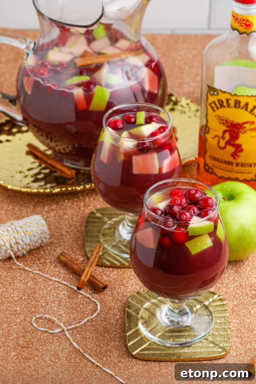 Cinnamon Spice Sangria 10 A pitcher and glasses filled with sangria, adorned with fresh fruit, set on a rustic wooden table, ready for serving.