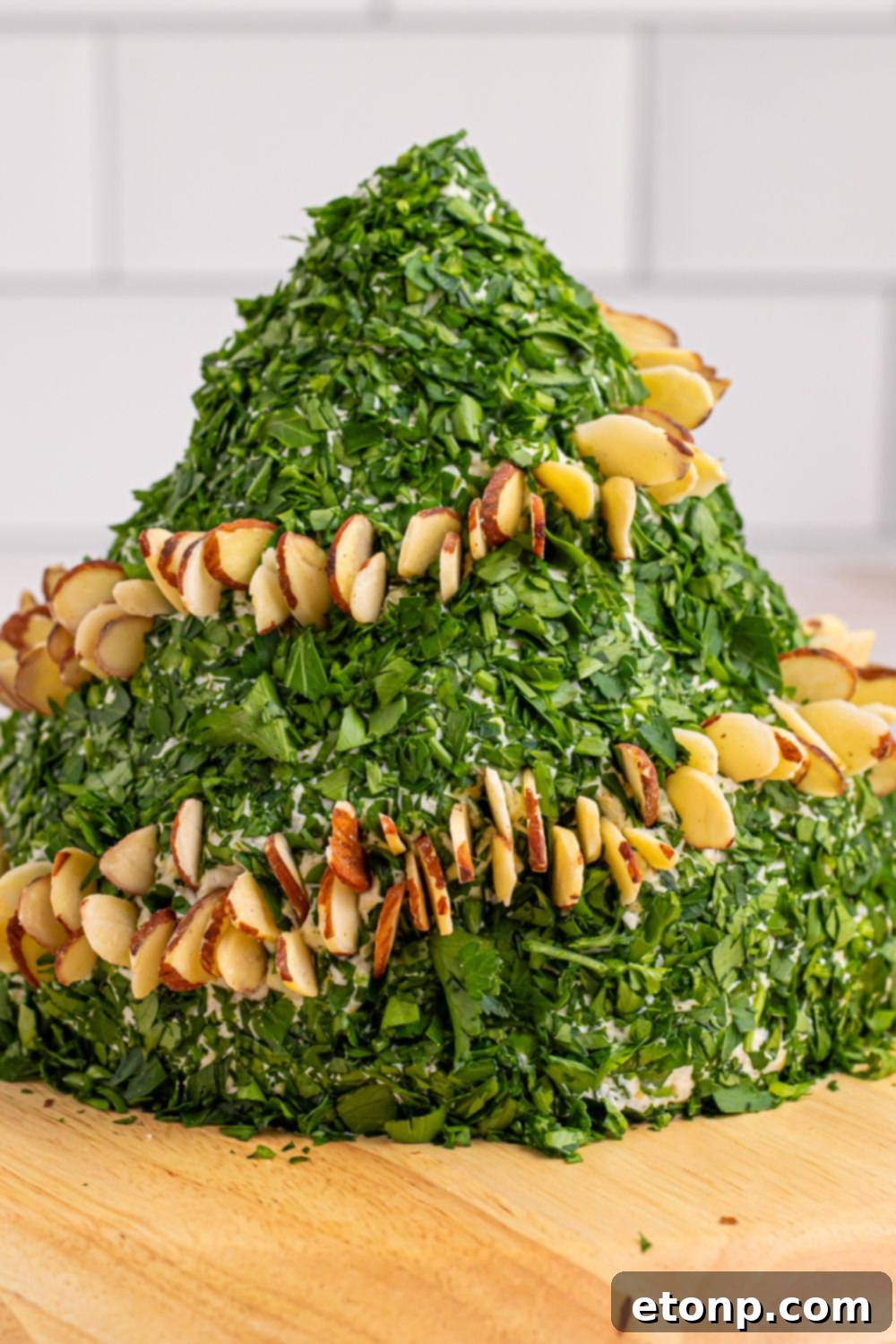 Side view of a cheeseball being decorated with almonds and peppers