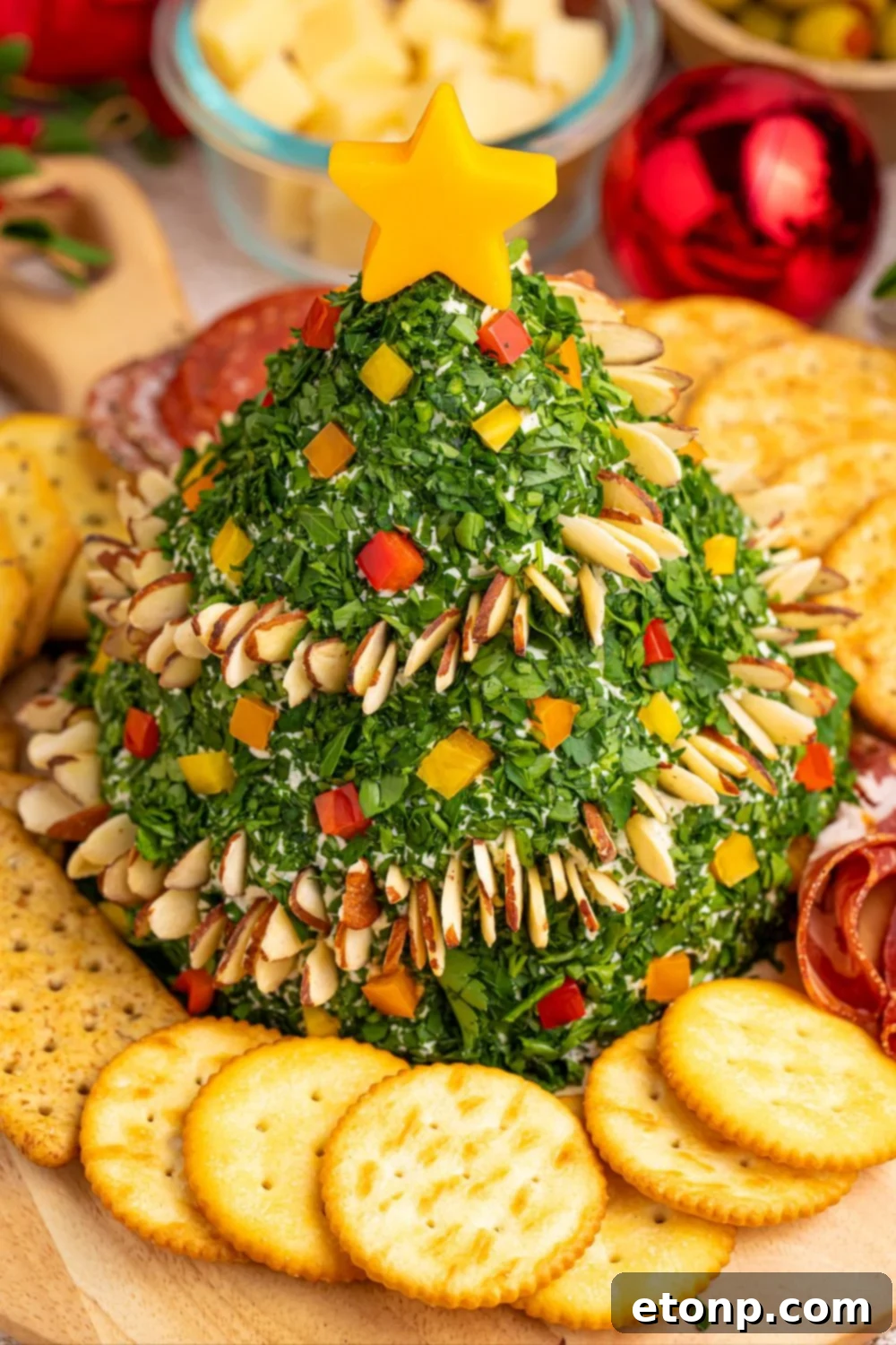 Side view of Christmas Tree Cheeseball on a board with crackers and grapes