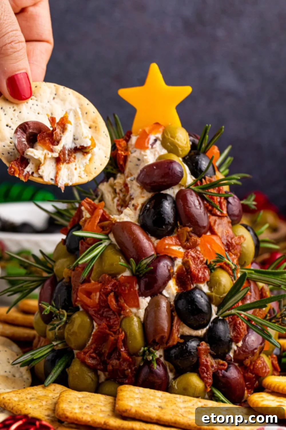 A delicious cracker topped with a generous spread of cheeseball mixture and a few olives, demonstrating a perfect bite.