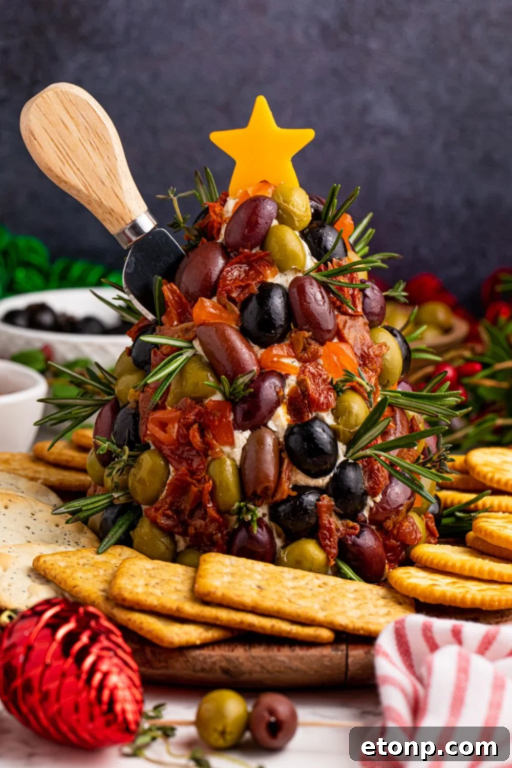 The Antipasto Christmas Tree Cheeseball, with a knife stuck into its side, illustrating its readiness to be served and enjoyed by guests.