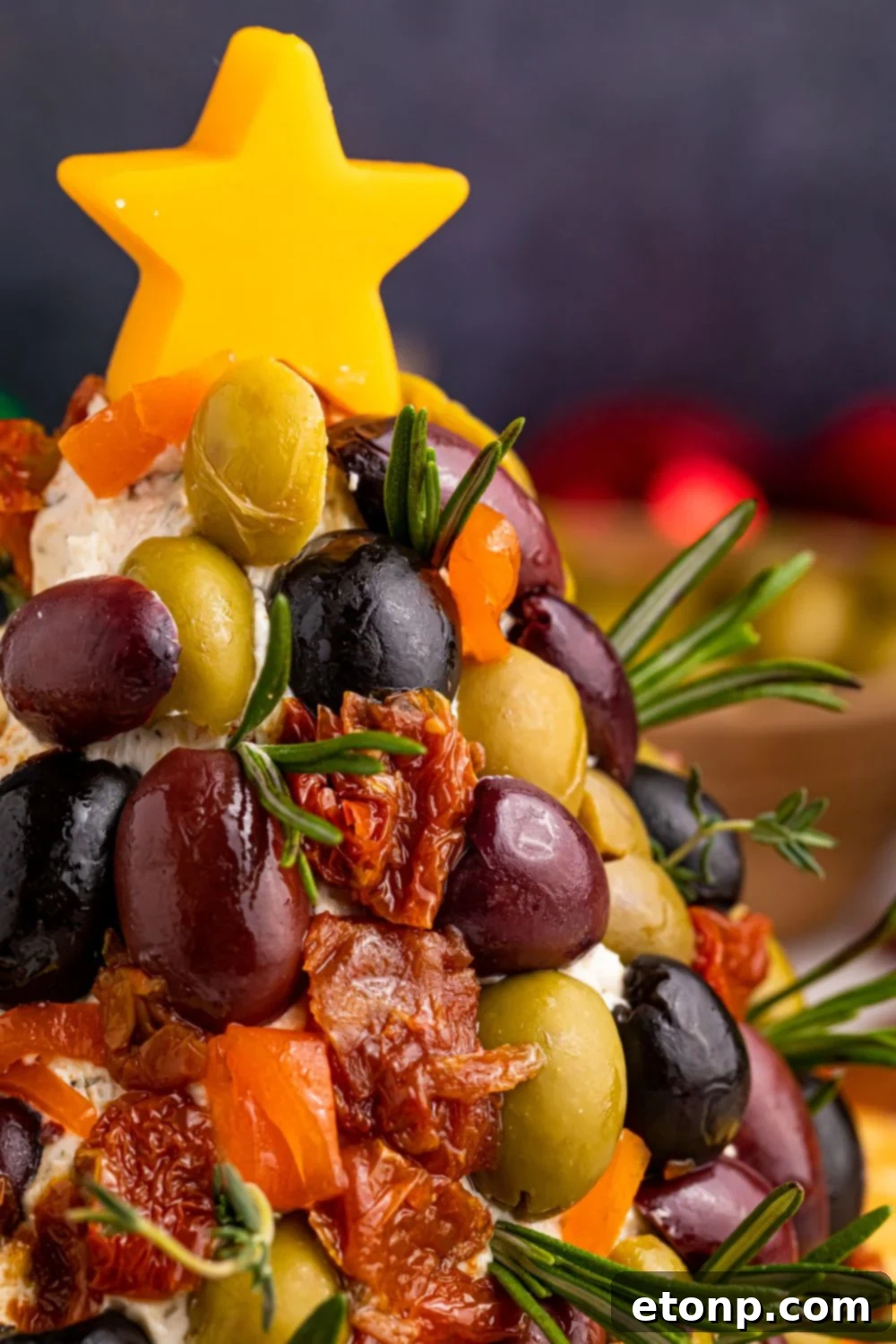 Close-up side view of the elaborately decorated Antipasto Christmas Tree Cheeseball, showcasing its vibrant olives and sundried tomatoes.