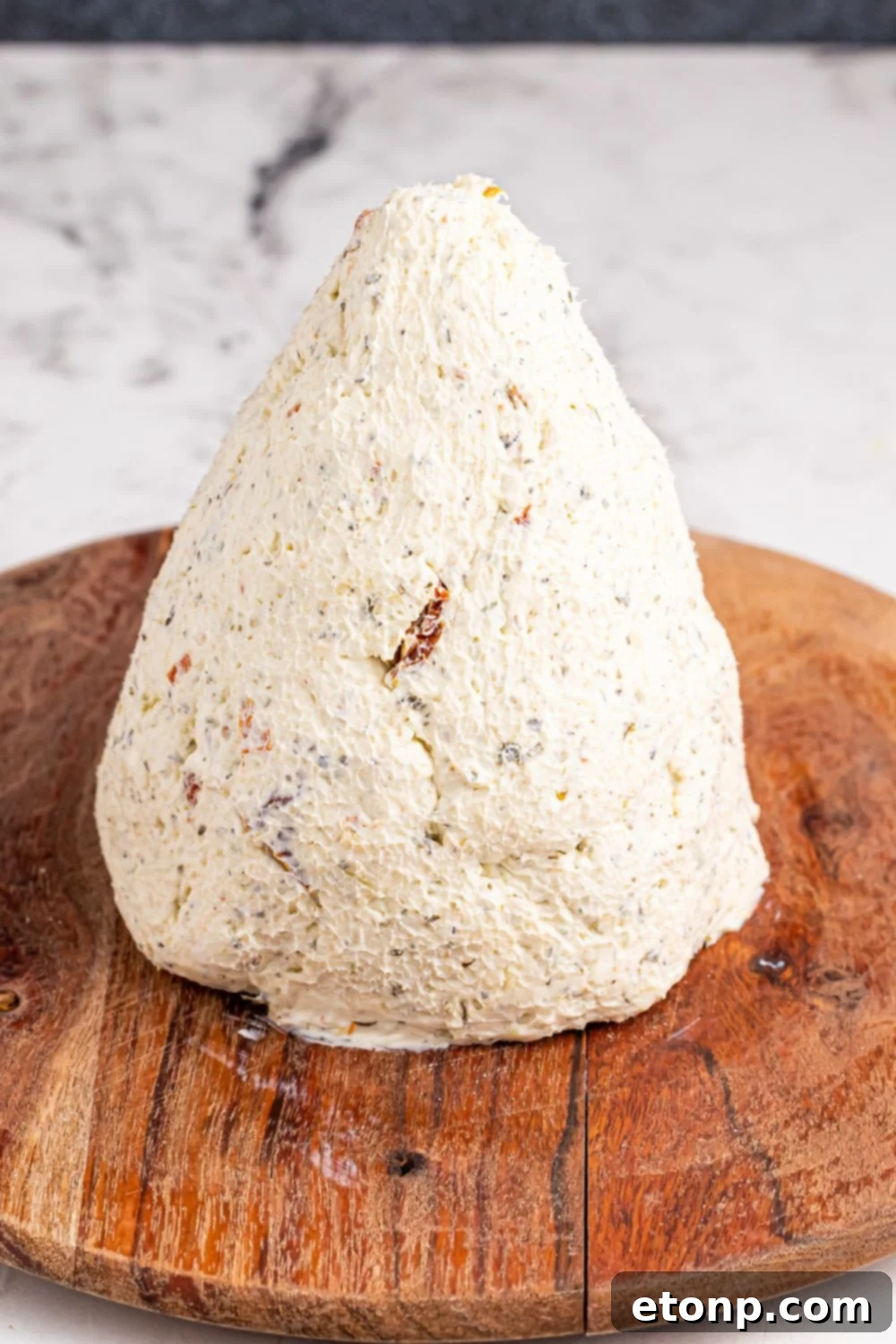 The cheeseball mixture, skillfully formed into a perfect cone shape, resting on a round cutting board, preparing for decoration.
