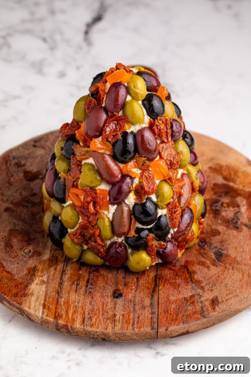 The festive cheeseball, meticulously decorated with a colorful array of olives and sun-dried tomatoes, creating a beautiful holiday design.