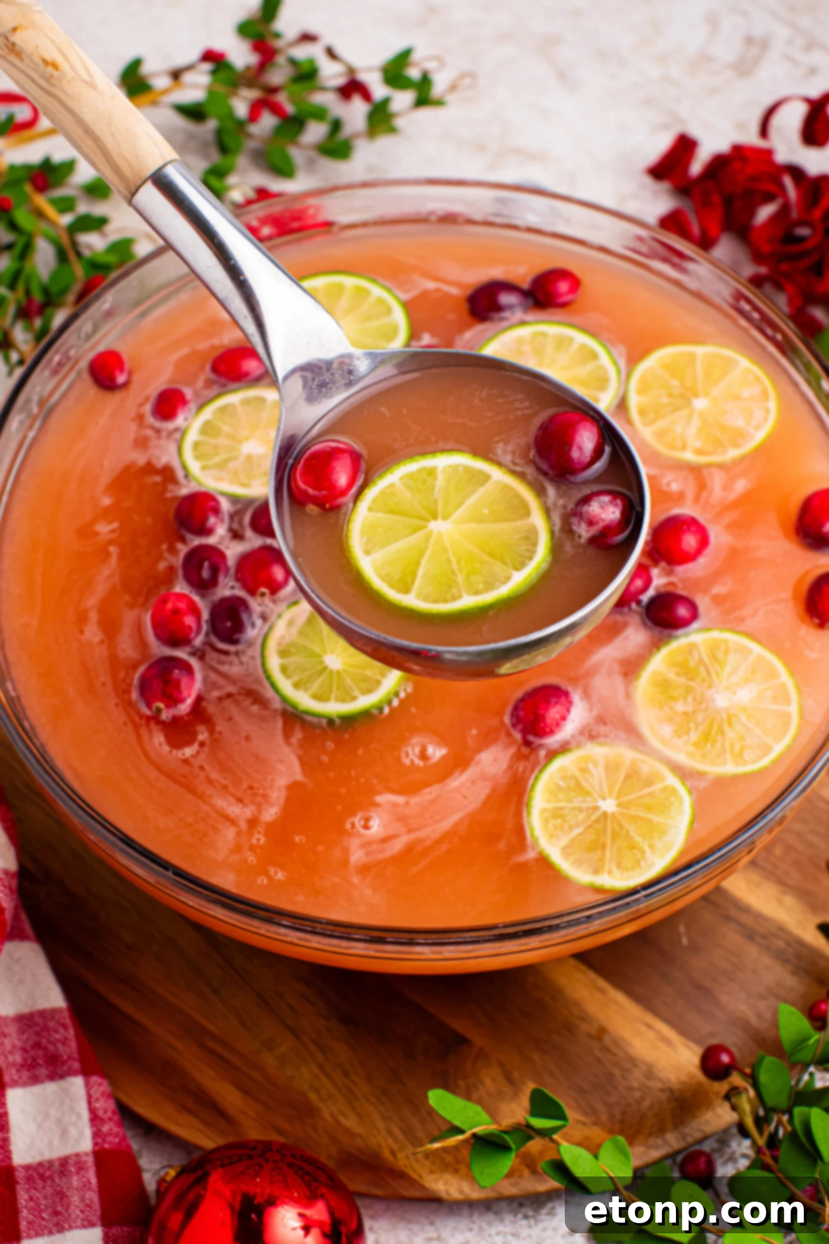 Large punch bowl filled with Santa's Giggle Juice, a vibrant Christmas sherbet punch, garnished with fresh cranberries and lime slices, with a serving ladle and a glass ready for enjoyment.