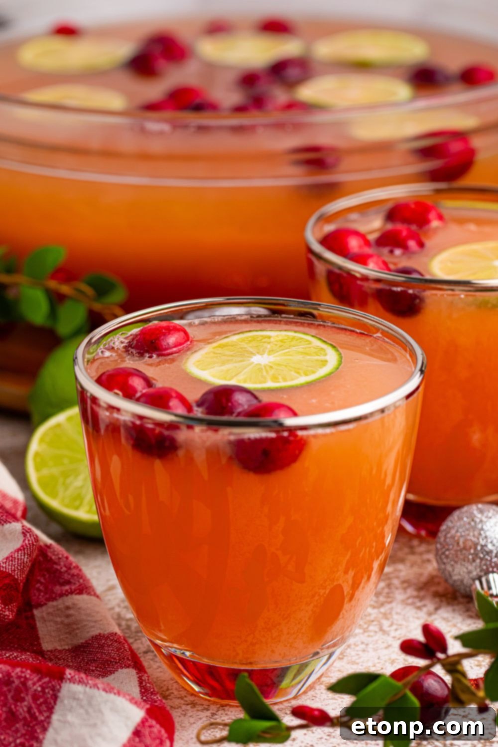 Multiple glasses of vibrant Santa's Giggle Juice Punch, garnished with cranberries and lime, neatly arranged on a festive table setting, ready for guests.