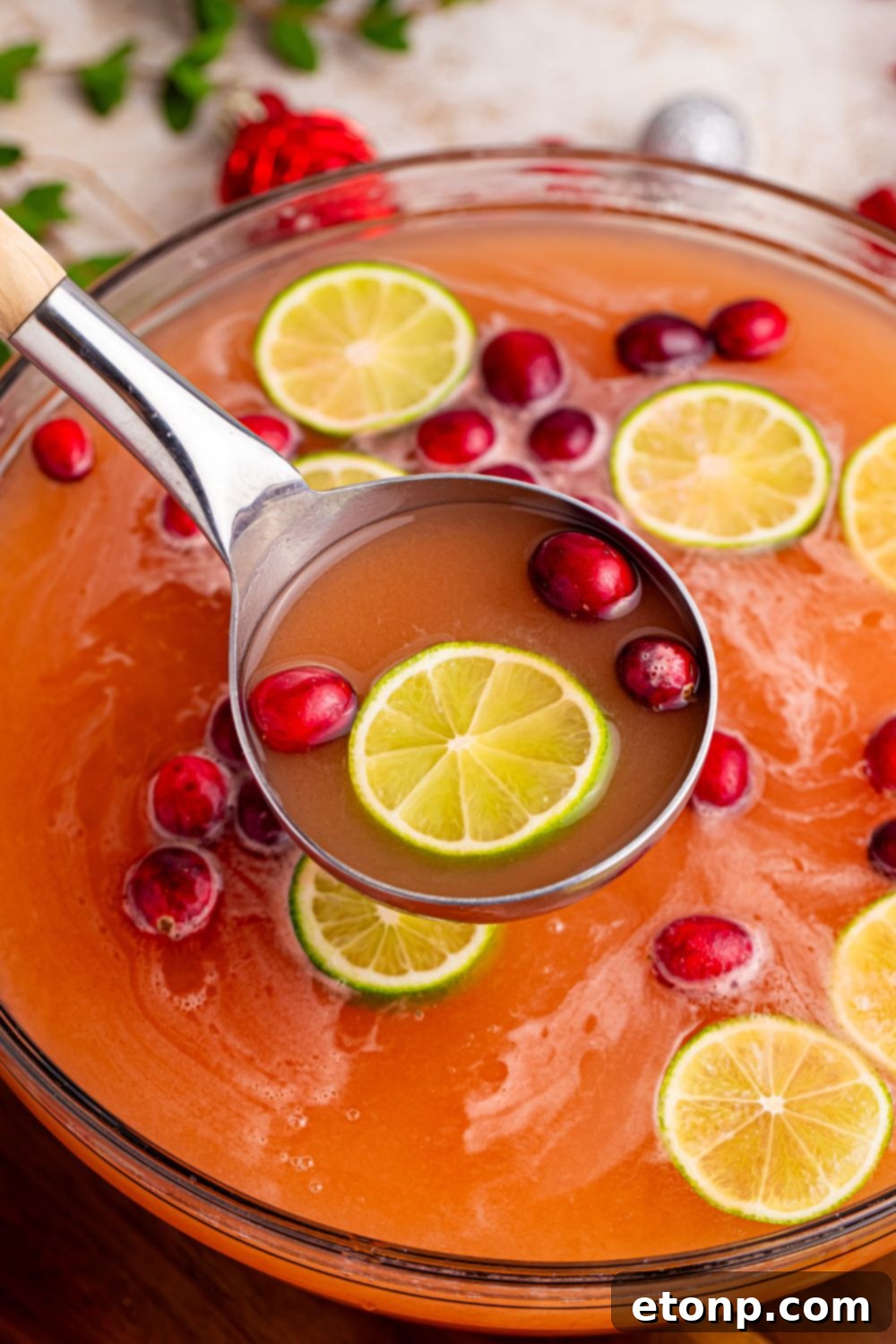 A festive punch bowl with Santa's Giggle Juice, showcasing melting sherbet and fresh fruit garnishes, with a serving ladle resting inside, ready for a holiday celebration.