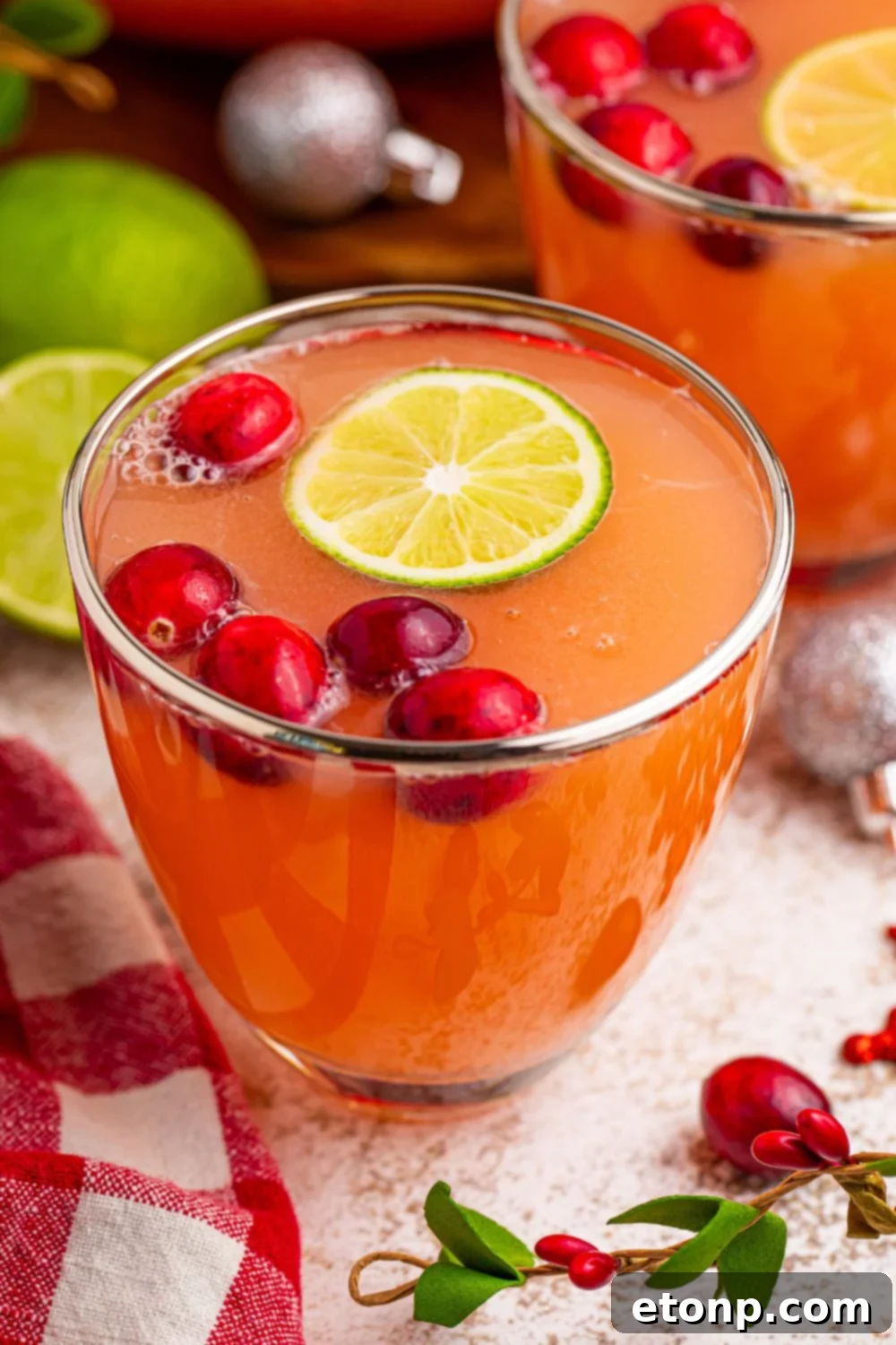 Close-up of a single glass filled with Santa's Giggle Juice Punch, highlighting the layered colors of the sherbet and juice, with a slice of lime on the rim, on a blurred background.