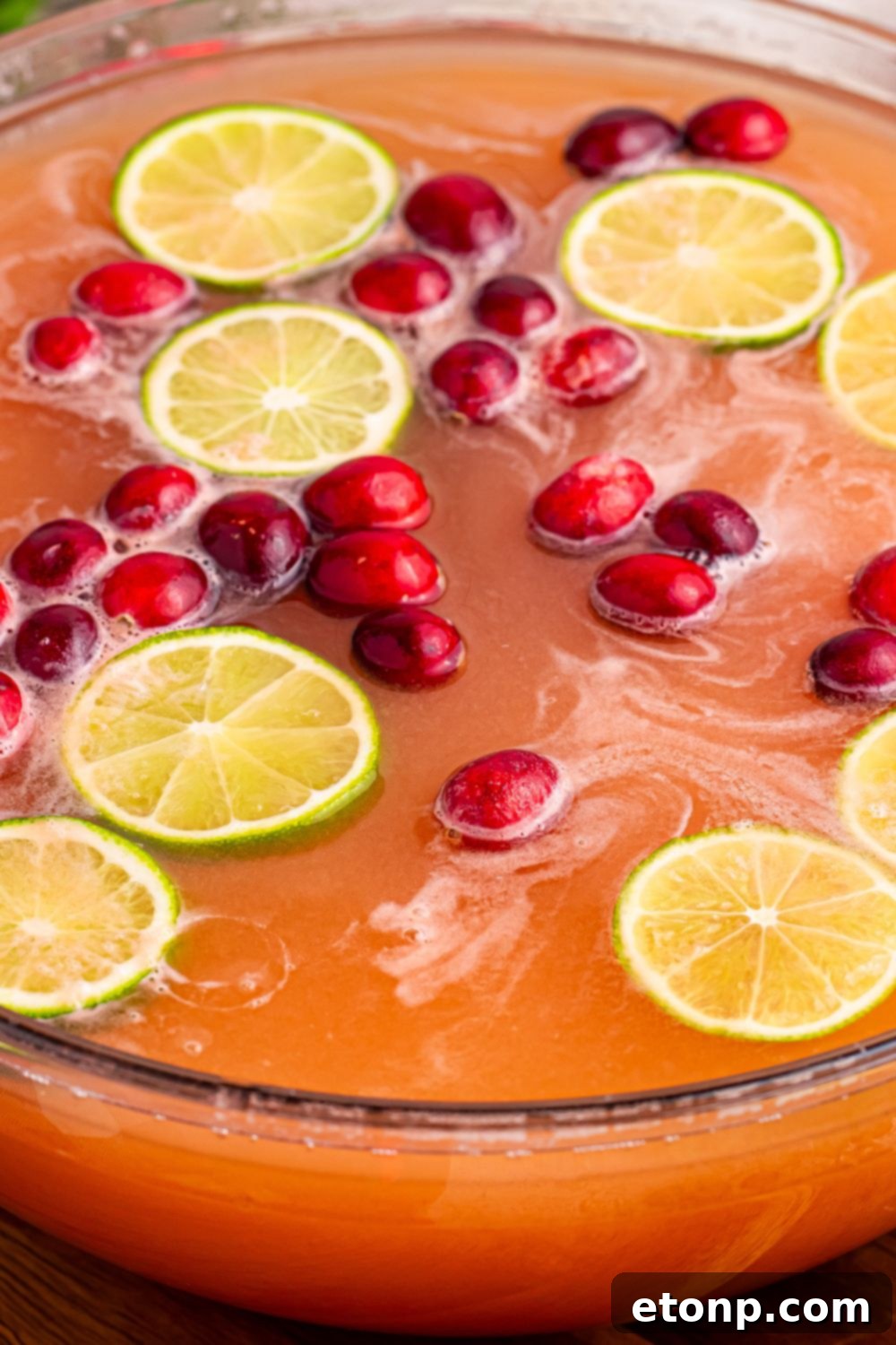 A large punch bowl filled with Santa's Giggle Juice Punch, generously garnished with fresh cranberries, lime slices, and scoops of sherbet, creating a visually appealing and delicious holiday drink.