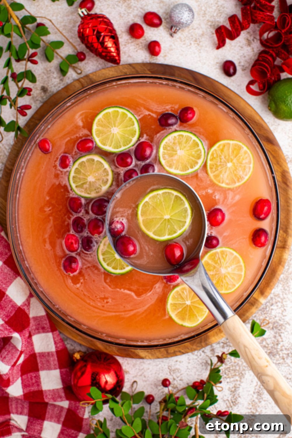 A serving ladle dipped into a large punch bowl of Santa's Giggle Juice, emphasizing the inviting texture and vibrant color of the festive holiday drink.