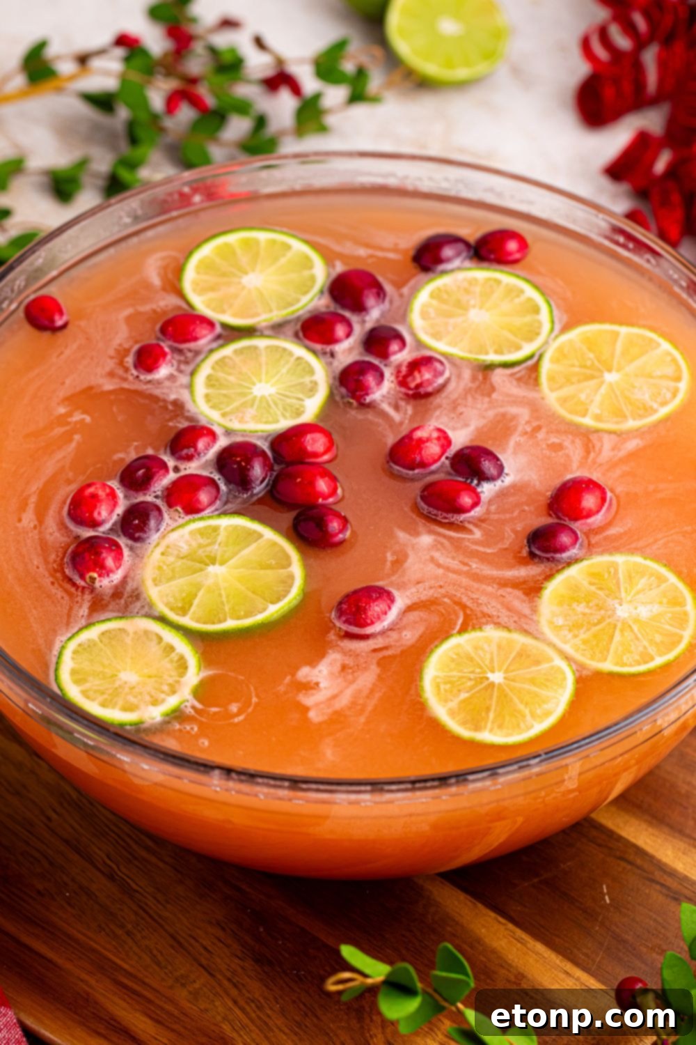A large, clear glass punch bowl filled with a festive Christmas cocktail punch, featuring vibrant red and green garnishes, ready for a holiday celebration.