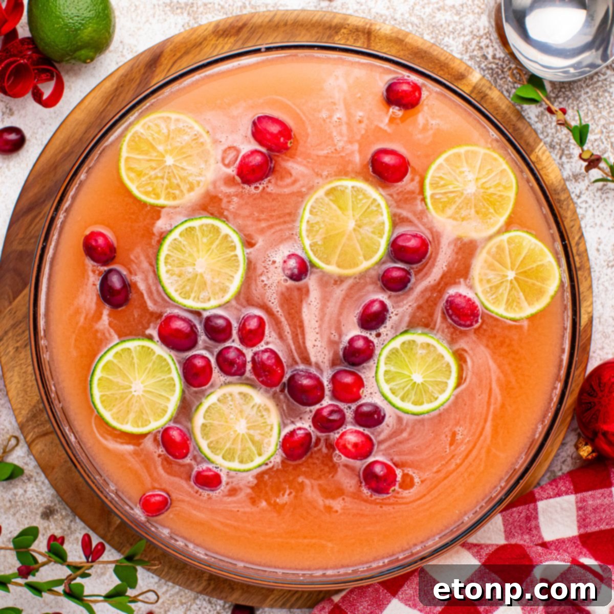 Overhead view of a beautifully presented Santa's Giggle Juice Punch in a large glass punch bowl, adorned with floating cranberries and lime, set on a rustic wooden table, ready for a holiday celebration.