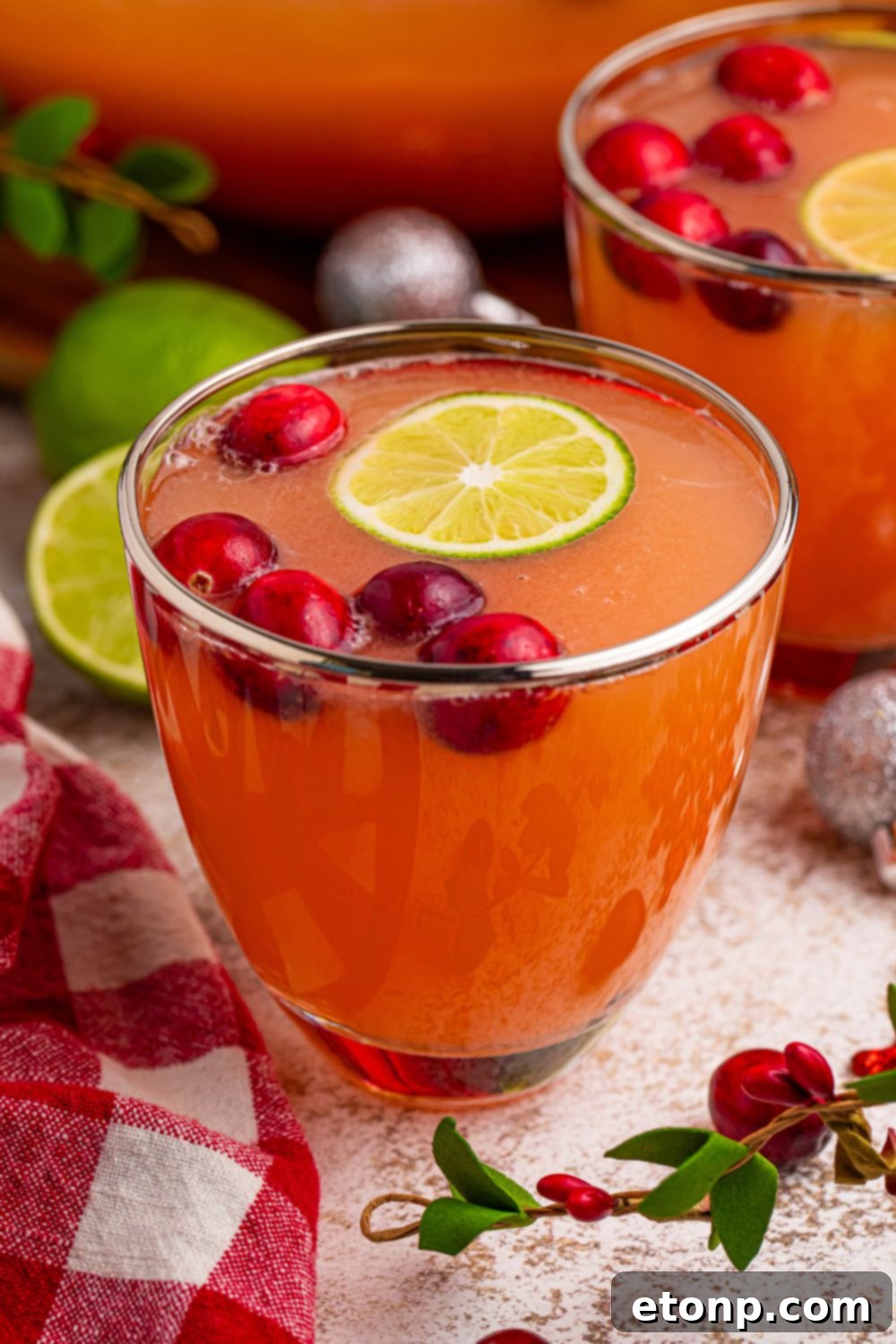 Close-up of individual glasses filled with Santa's Giggle Juice Punch, garnished with fresh cranberries and lime wheels, artfully arranged on a festive holiday table.
