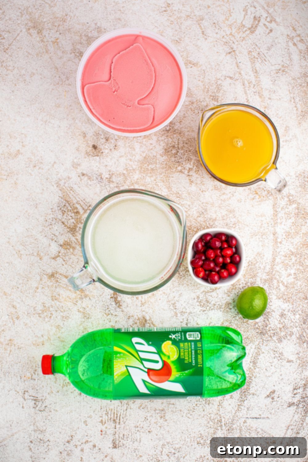 A collection of fresh ingredients for Santa's Giggle Juice Punch, including limeade bottles, various sherbet containers, pineapple juice, and a 2-liter bottle of 7UP, neatly arranged on a kitchen counter.