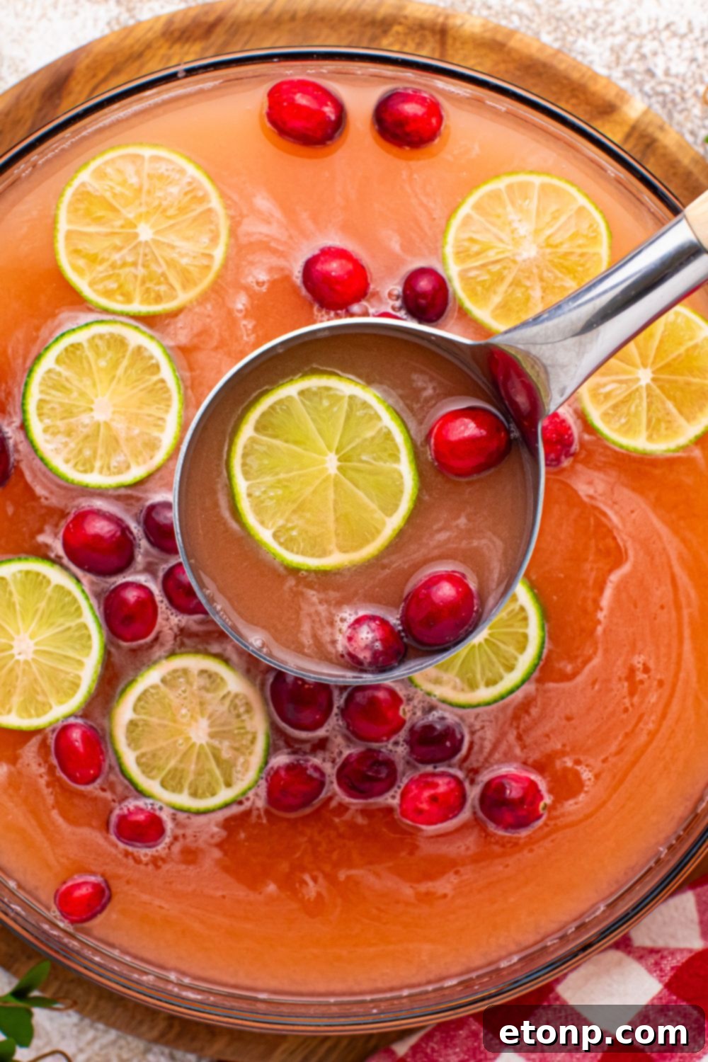 Close-up of a large, clear glass punch bowl filled with a vibrant pink Christmas punch, topped with scoops of melting raspberry sherbet, and garnished with fresh lime slices and cranberries.