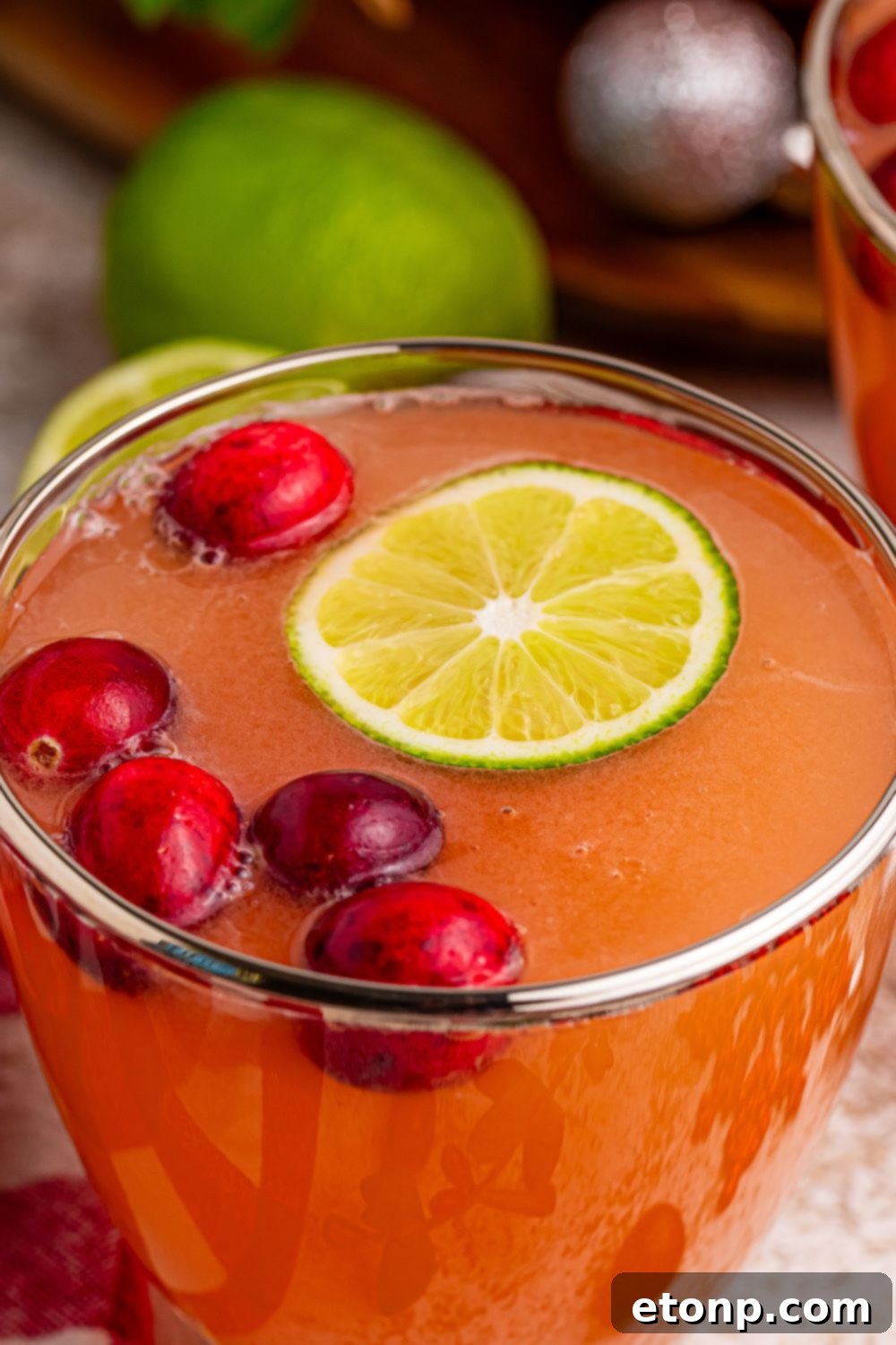 Individual glass of Santa's Giggle Juice Punch, showcasing the frothy pink sherbet, vibrant lime slices, and fresh cranberries, ready to be enjoyed.