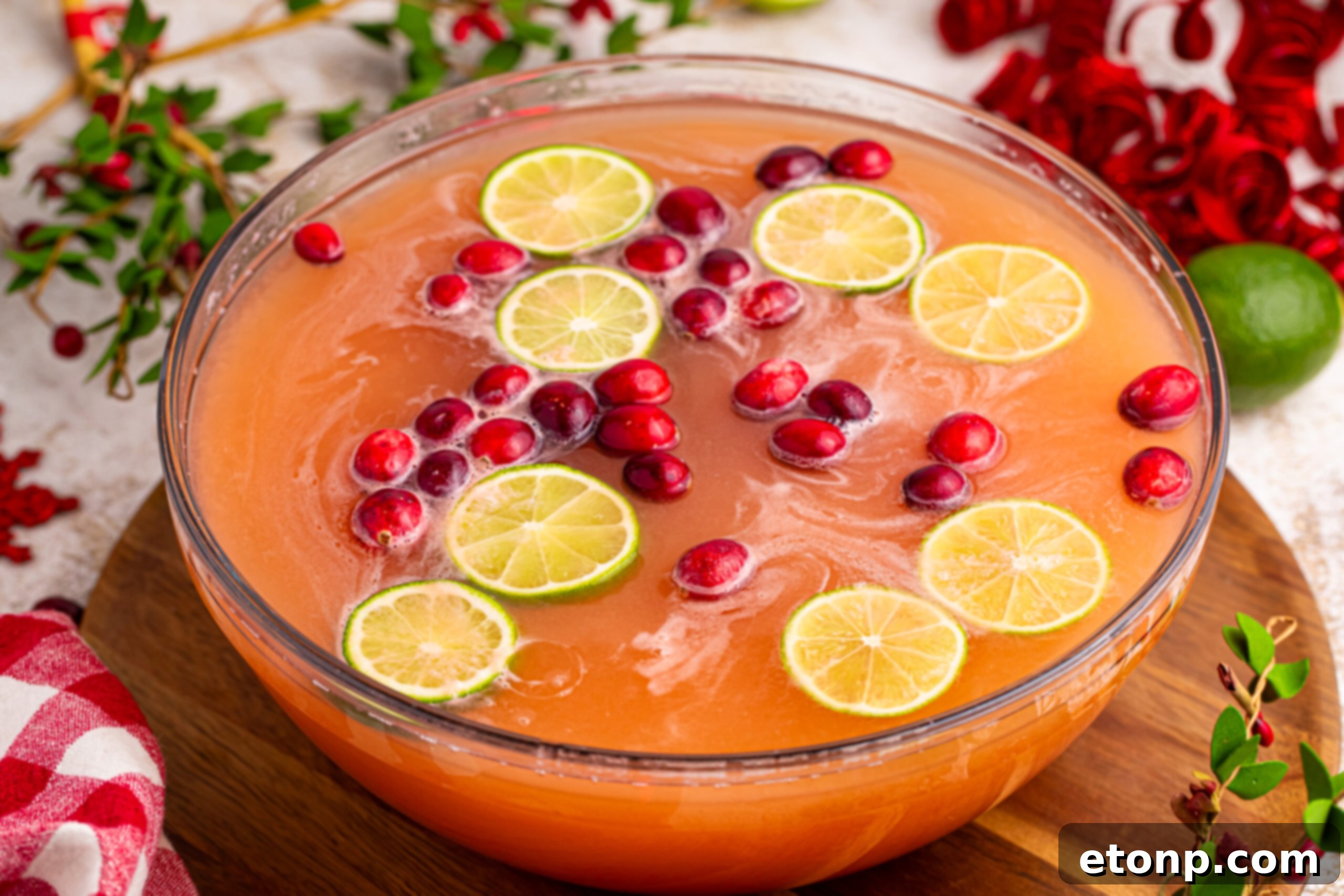 A large, ornate punch bowl brimming with Santa's Giggle Juice, garnished with vibrant fruit, prominently displayed on a wooden table, creating an inviting focal point for holiday entertaining.