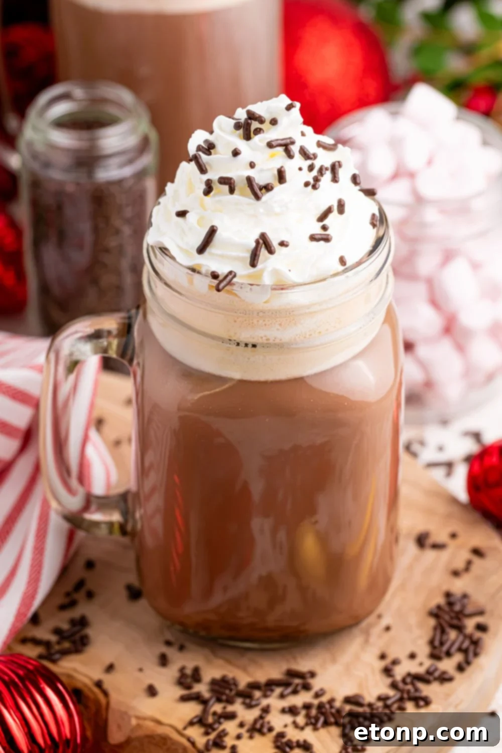 Naughty Snowman's Brew 14 Dirty snowman cocktail in a glass on a wooden coaster with sprinkles and whipped cream on top. There is a red and white towel and other Christmas decor behind the glass