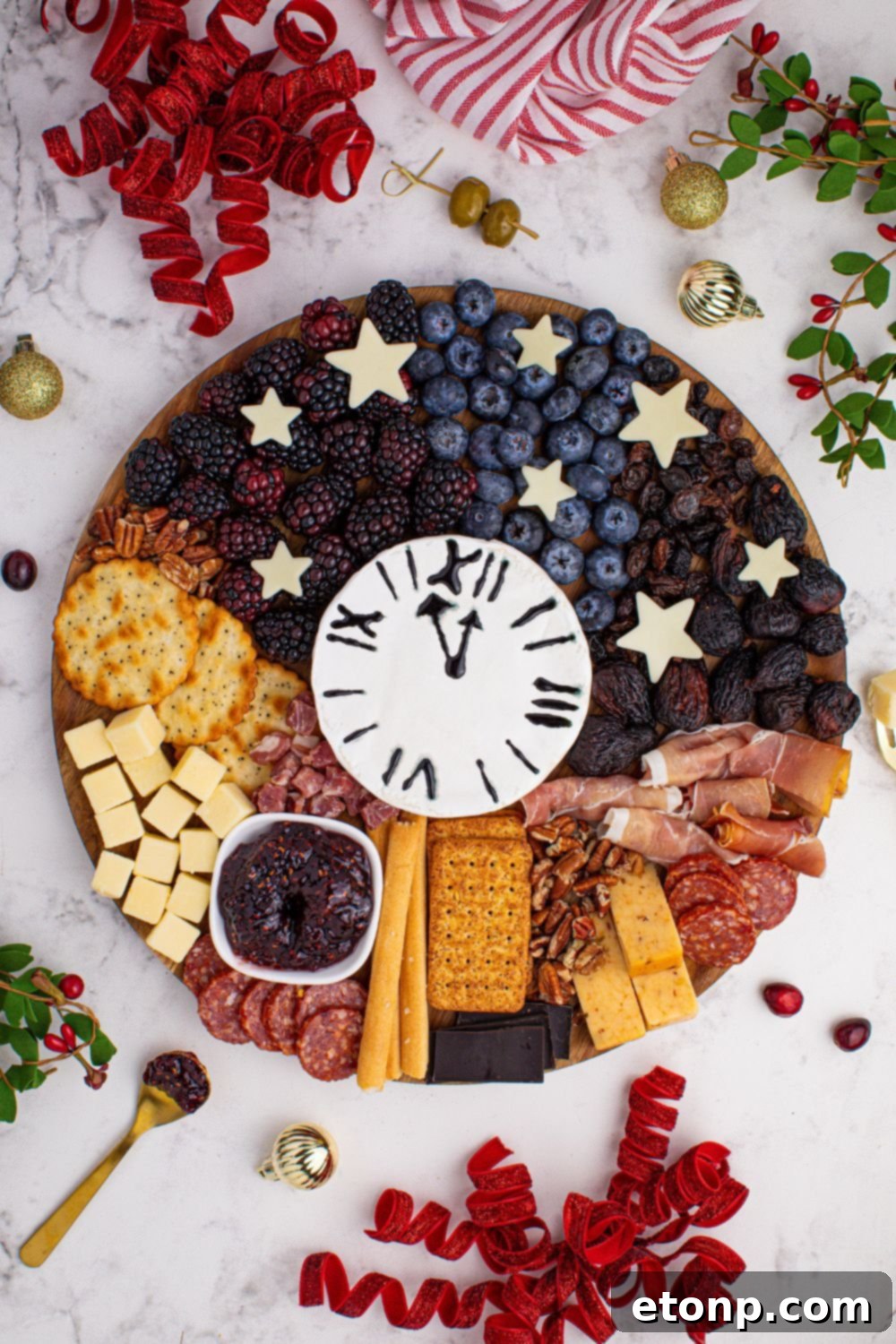 New Year's Eve Charcuterie Board on table with ribbon, berries and herbs around the table 