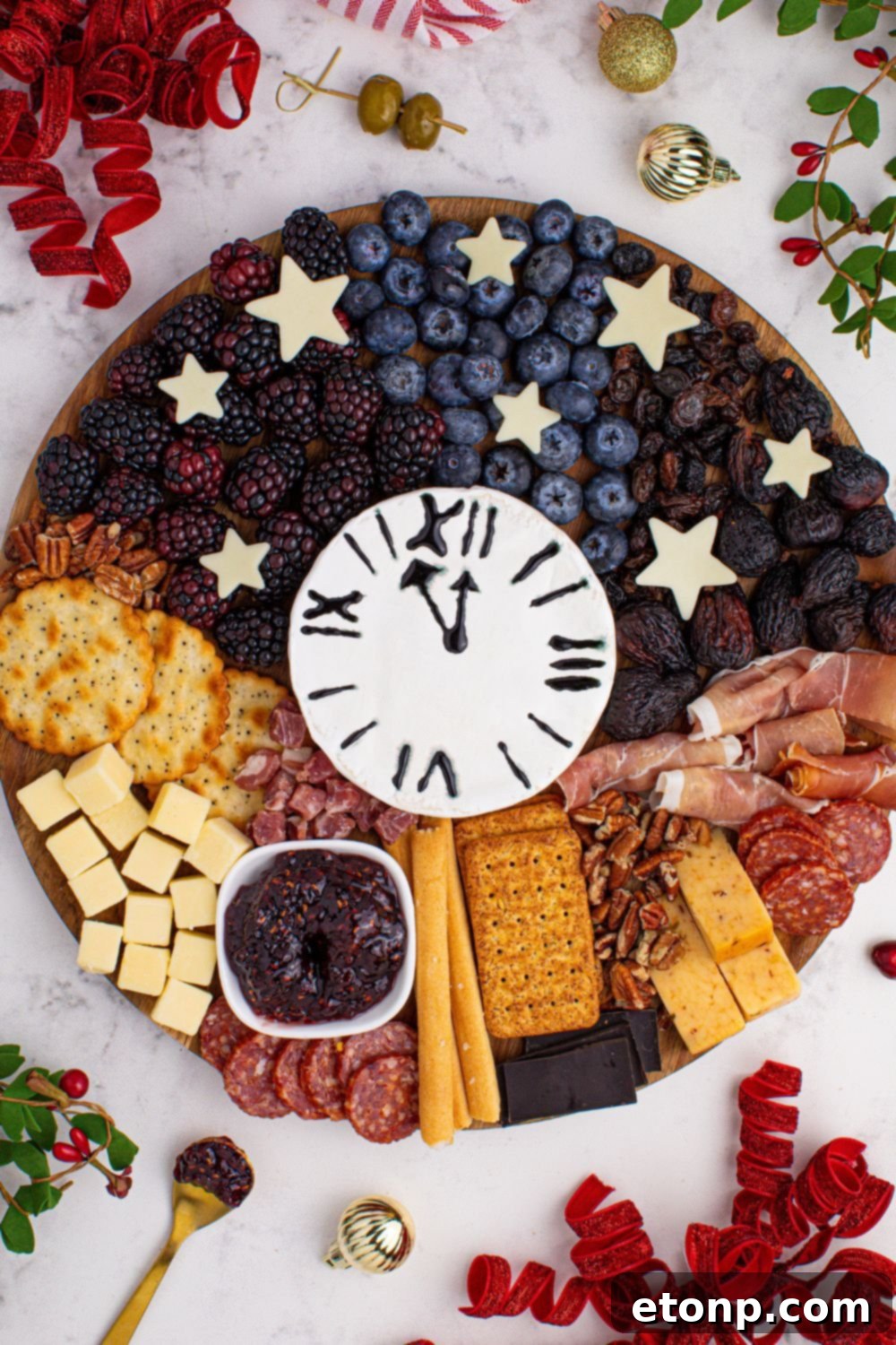 New Year's Eve Charcuterie Board sitting on table with CHristmas decor around it and some fruits on table 