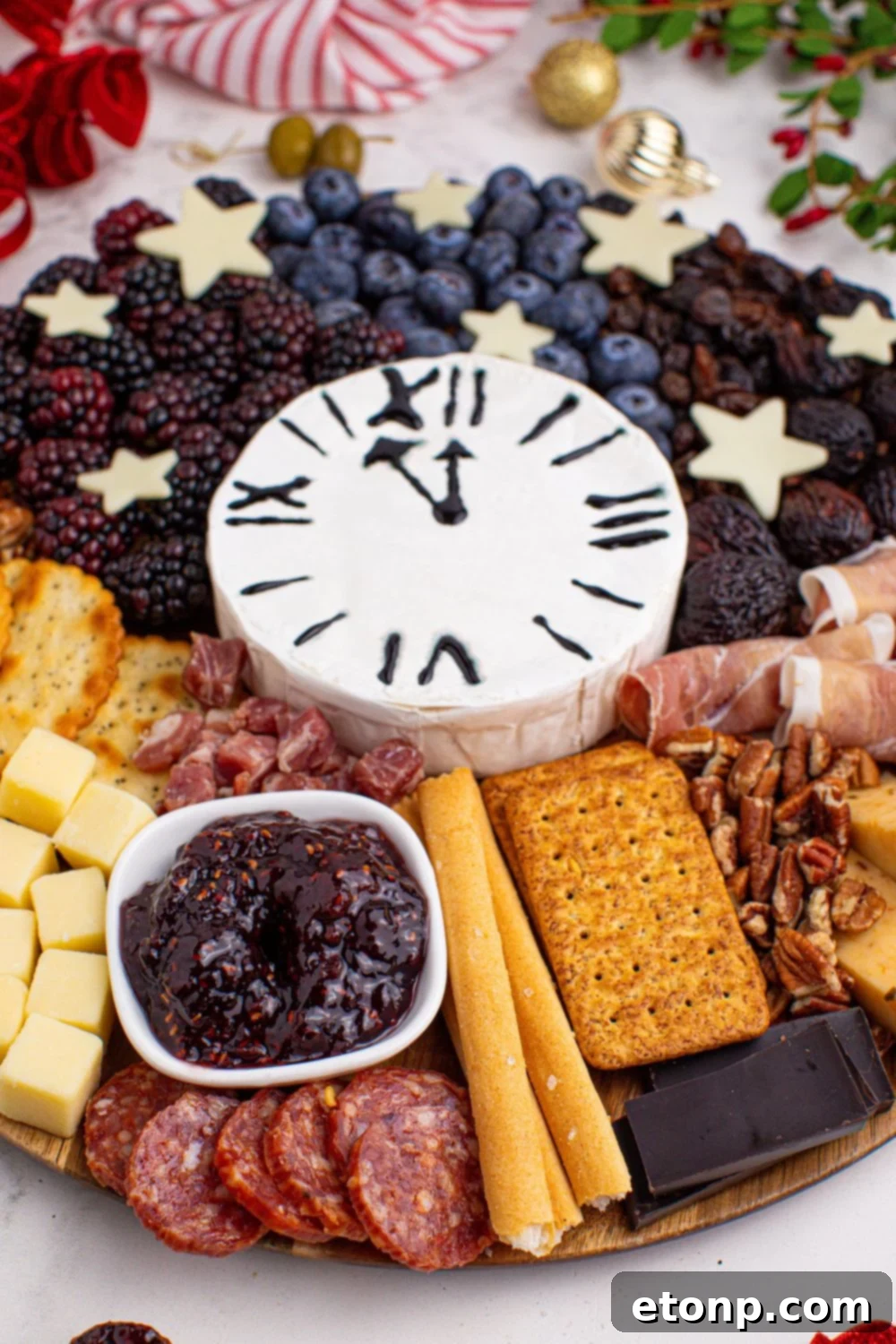 New Year's Eve Charcuterie Board that is on a table with some Christmas decor around the round charcuterie board 