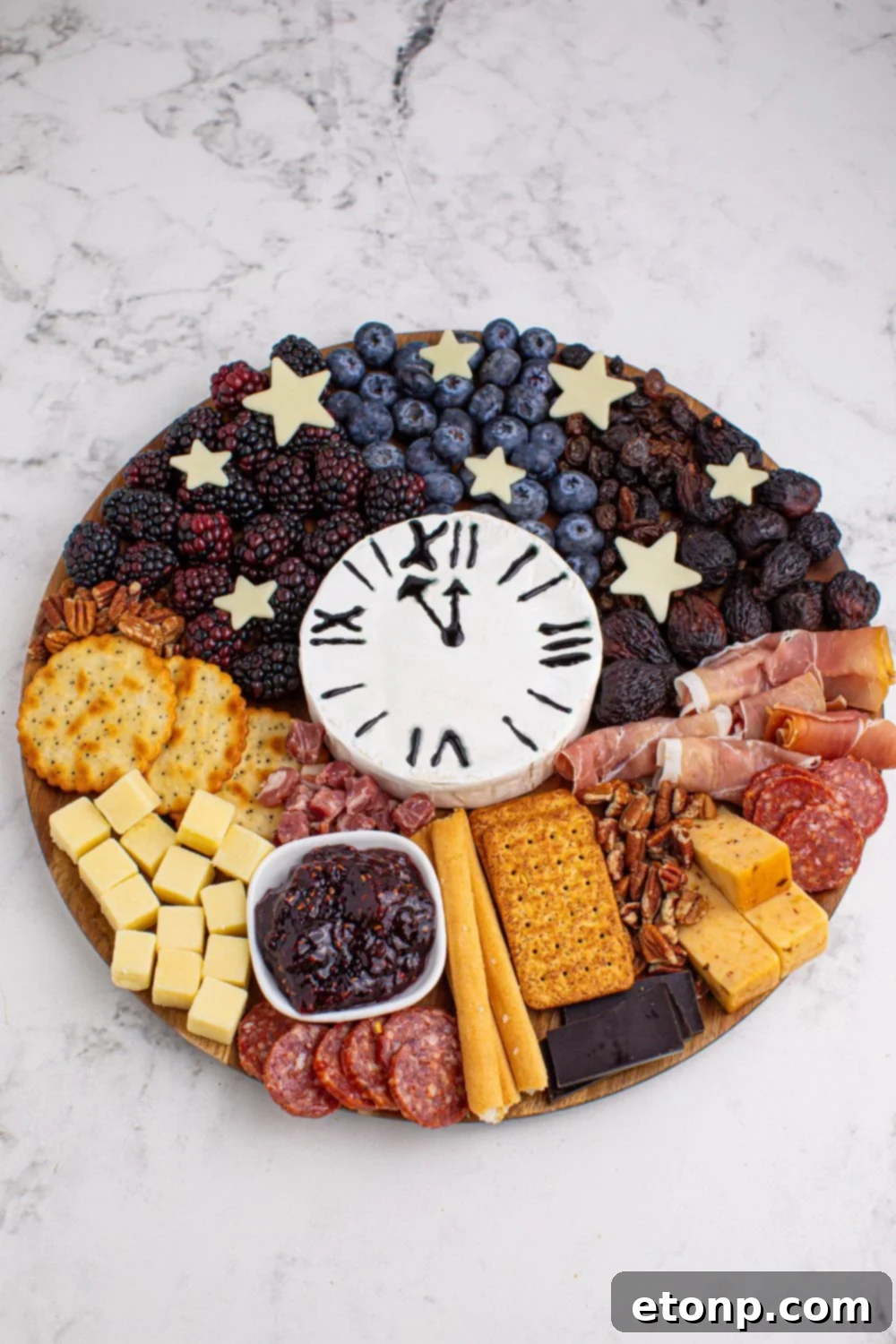 New Year's Eve Charcuterie Board on a marble table showcasing all the snacking items on the board with a brie bock in center that looks like a clock 