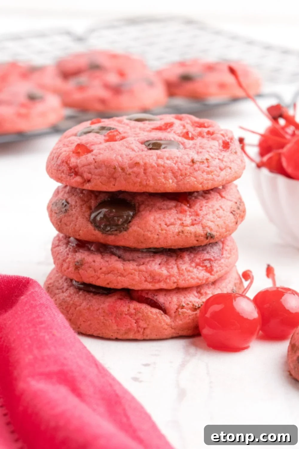 stacked Cherry Chocolate Chip Cookies on the table with two cherries sitting by it 